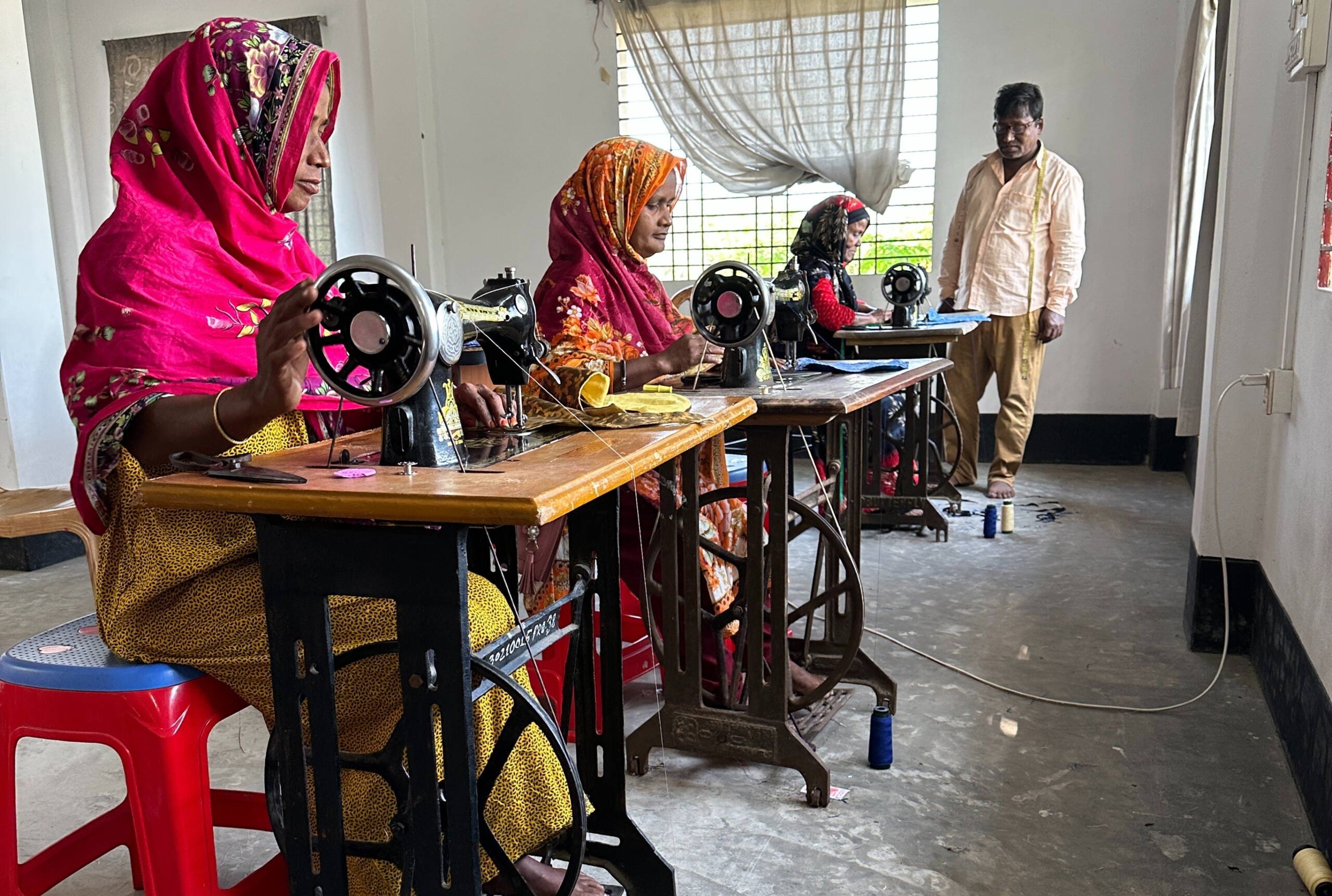 Lätzliproduktion Drei Fraun nähen, ein Mann steht dahinter und schaut zu.