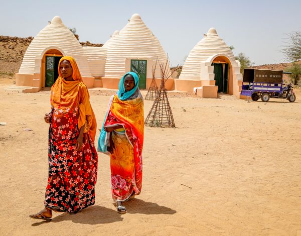 Zwei schwangere Frauen, dahinter ein mehrkuppliges Geburtshaus.
