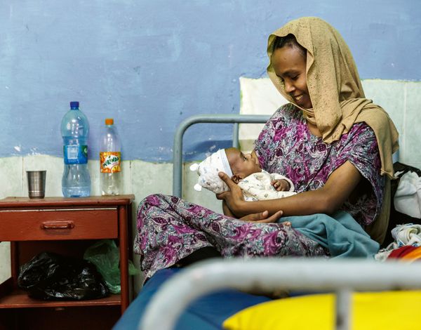 Eine Frau sitzt auf einem Spitalbett und schaut ihr Baby an.