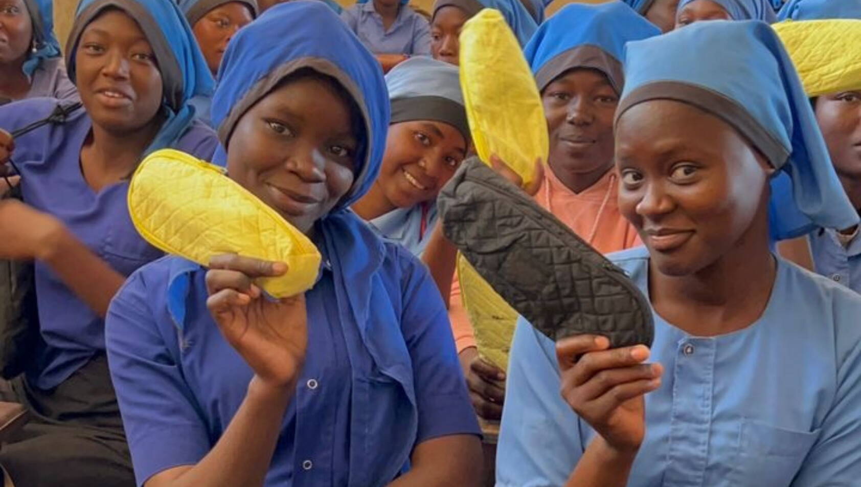 Verteilung Hygieneprodukte Mädchen in blauer Schuluniform halten stolz wiederverwendbare Binden in die Höhe.