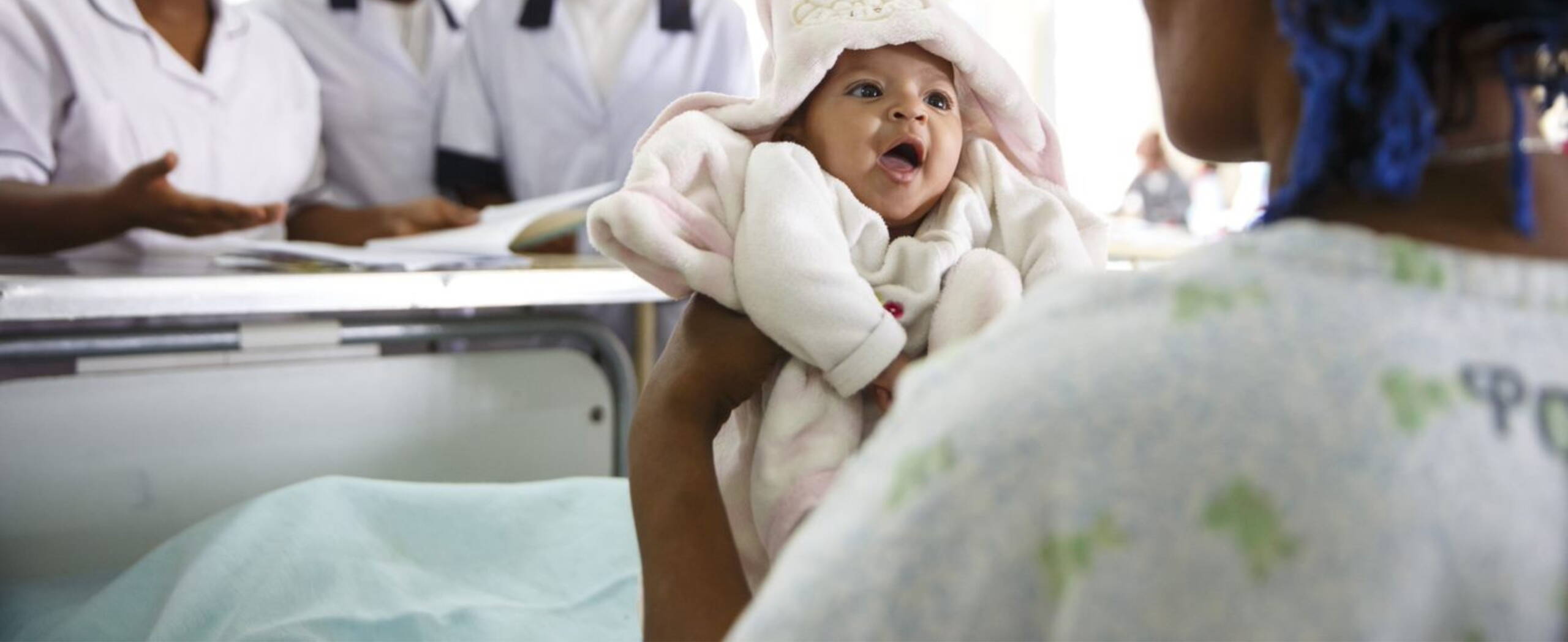 Ein Neugeborenes schaut interessiert ins Gesicht einer Frau, das es hochhält.