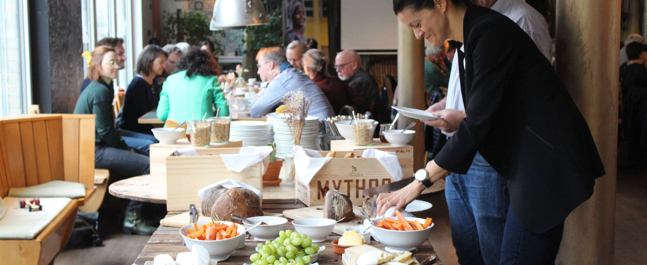 Jubiläumsbrunch Eine Frau bedient sich am Buffet, dahinter sind verschiedene Personen zu sehen, die sich angeregt unterhalten.