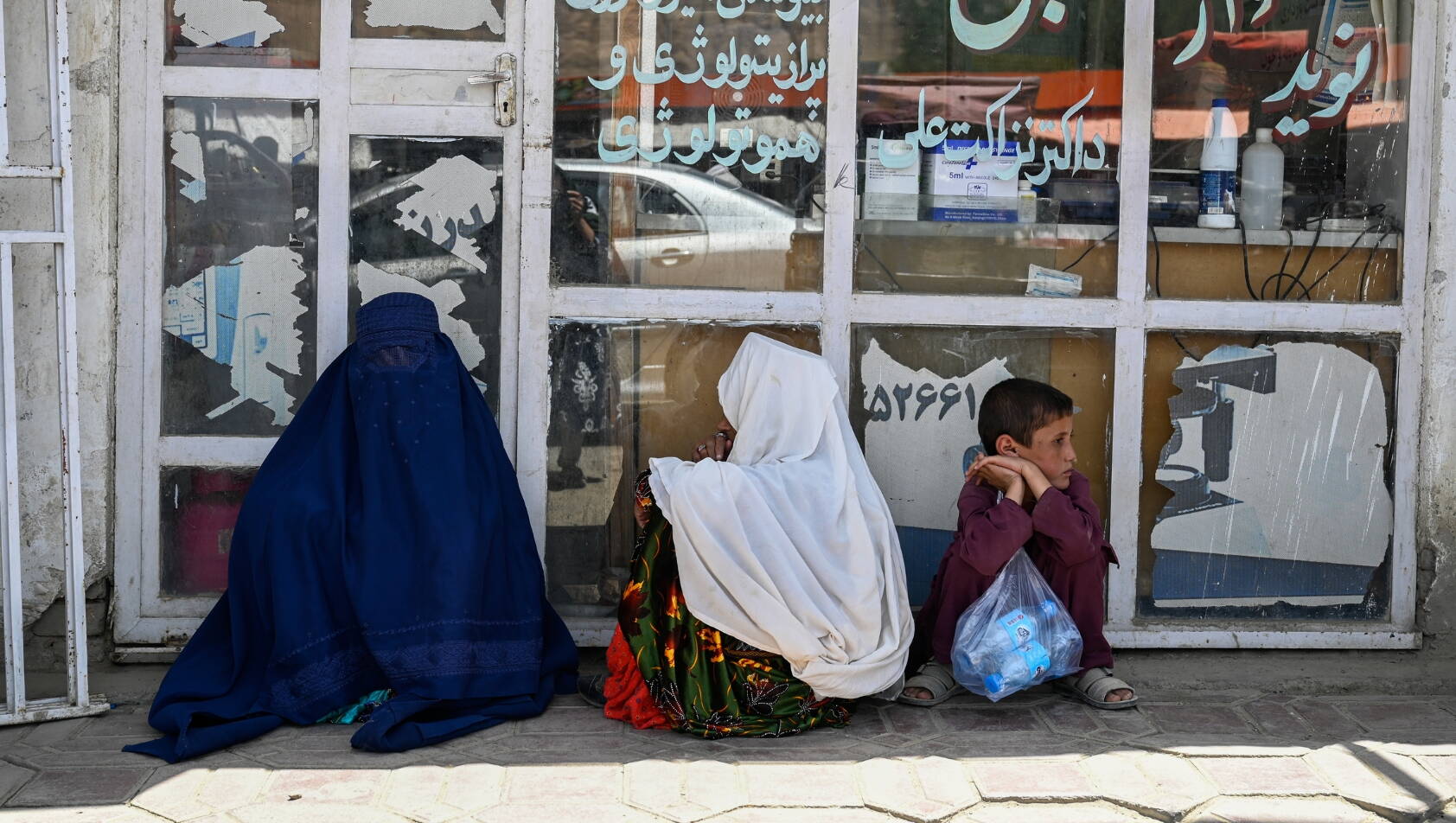 Eine Familie sitzt vor einer Gesundheitsklinik in Afghanistan, dir Frau bedeckt durch eine Burqa.