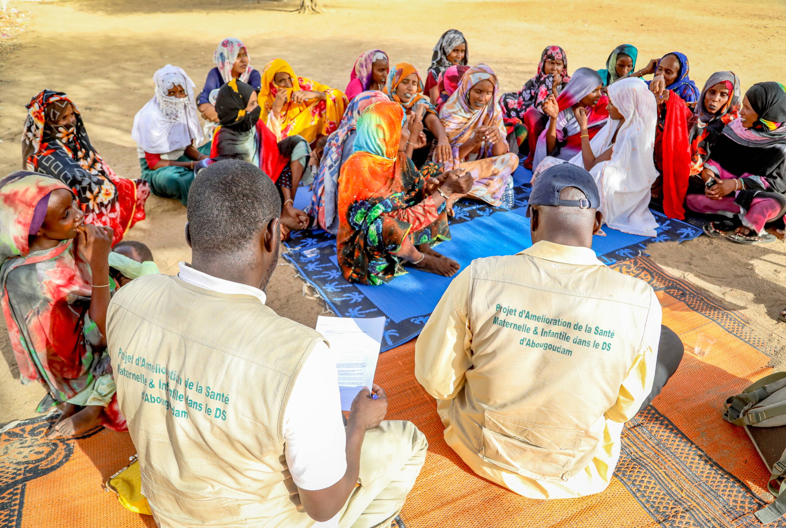 Zwei Mitarbeiter der Partnerorganisation BASE sitzen am Boden und befragen Frauen, die ebenfalls am Boden sitzen.