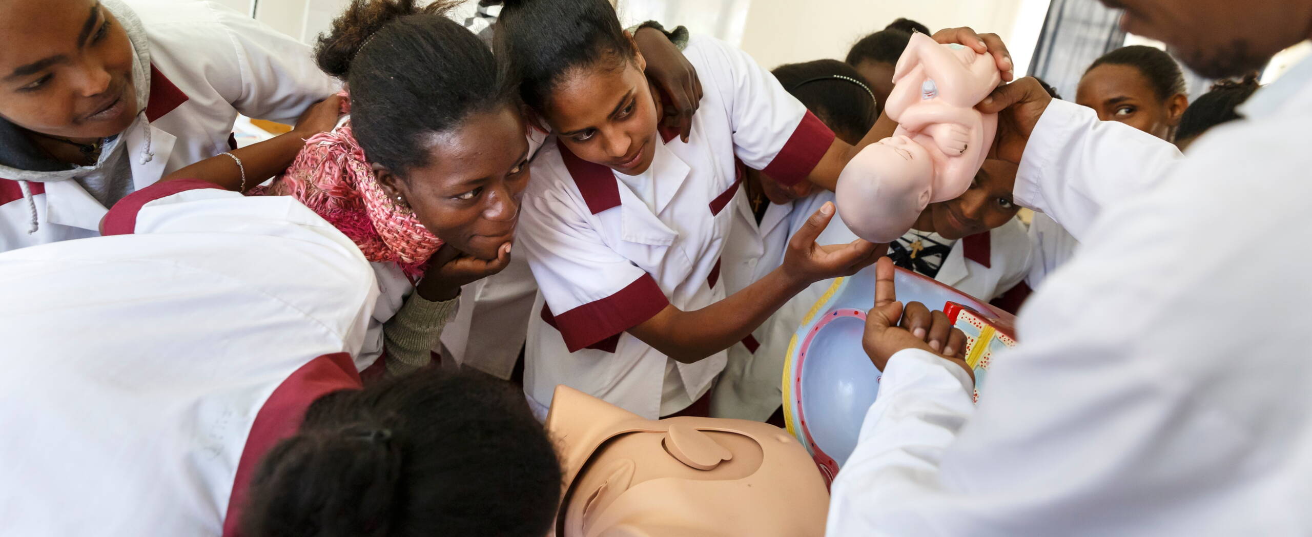 Hebammenausbildung Zwei Mädchen aus Afghanistan stehen sich gegenüber, eines trägt einen Kessel auf dem Kopf, das andere hält ihn.