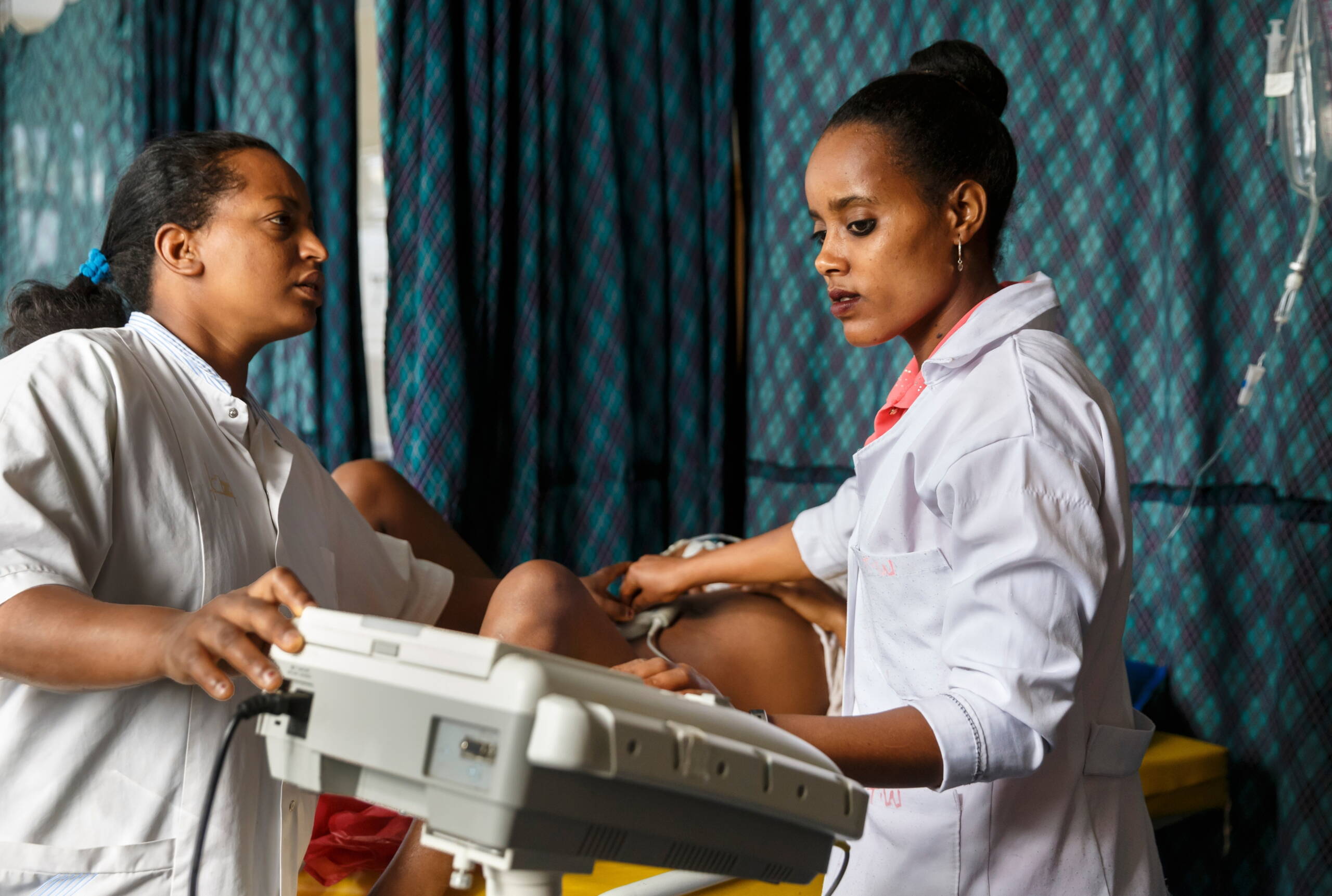 Zwei Frauen in weissen Kitteln führen bei einer schwangeren Frau einen Ultraschall durch.