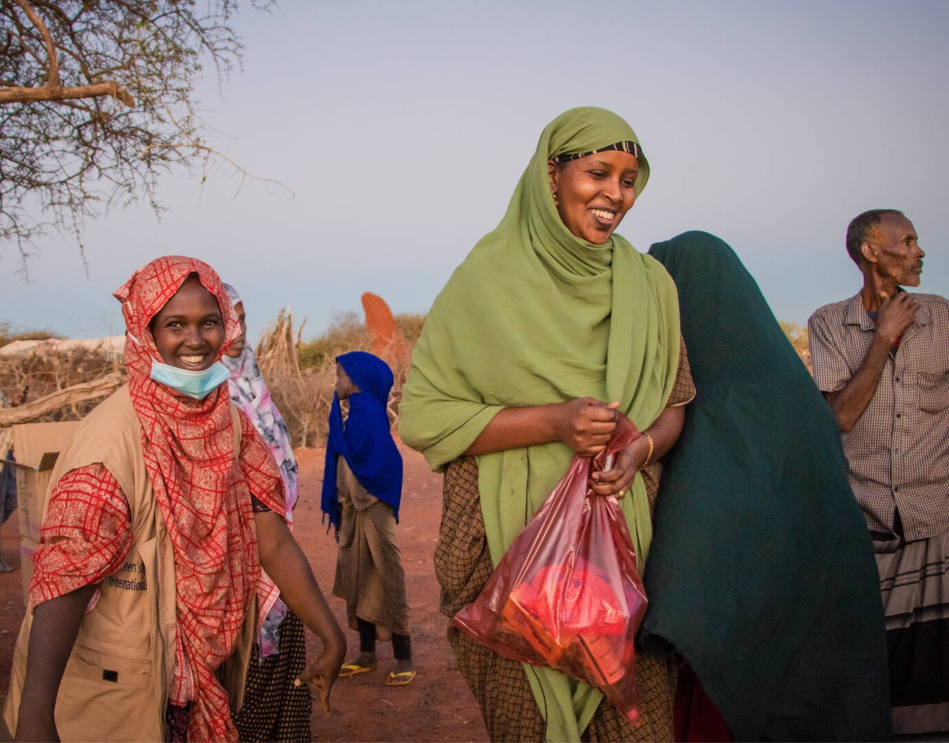 Eine Frau hält einen Sack mit verschiedenen Produkten in der Hand und lächelt, daneben eine Mitarbeiterin von OWDA, die den Sack übergeben hat.