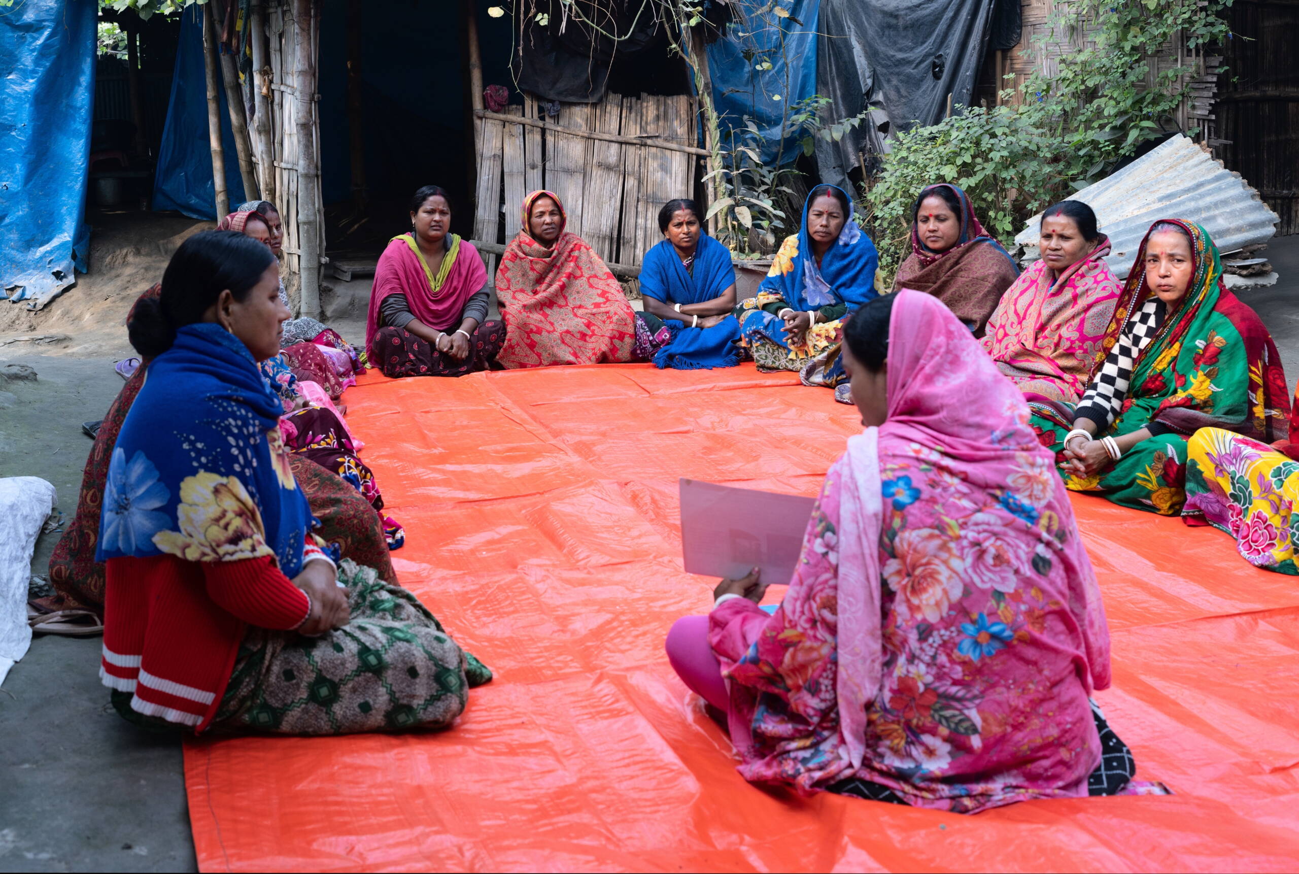 Frauen sitzen am Boden und tauschen sich aus, eine Frau erzählt etwas und hält ein Papier in der Hand.