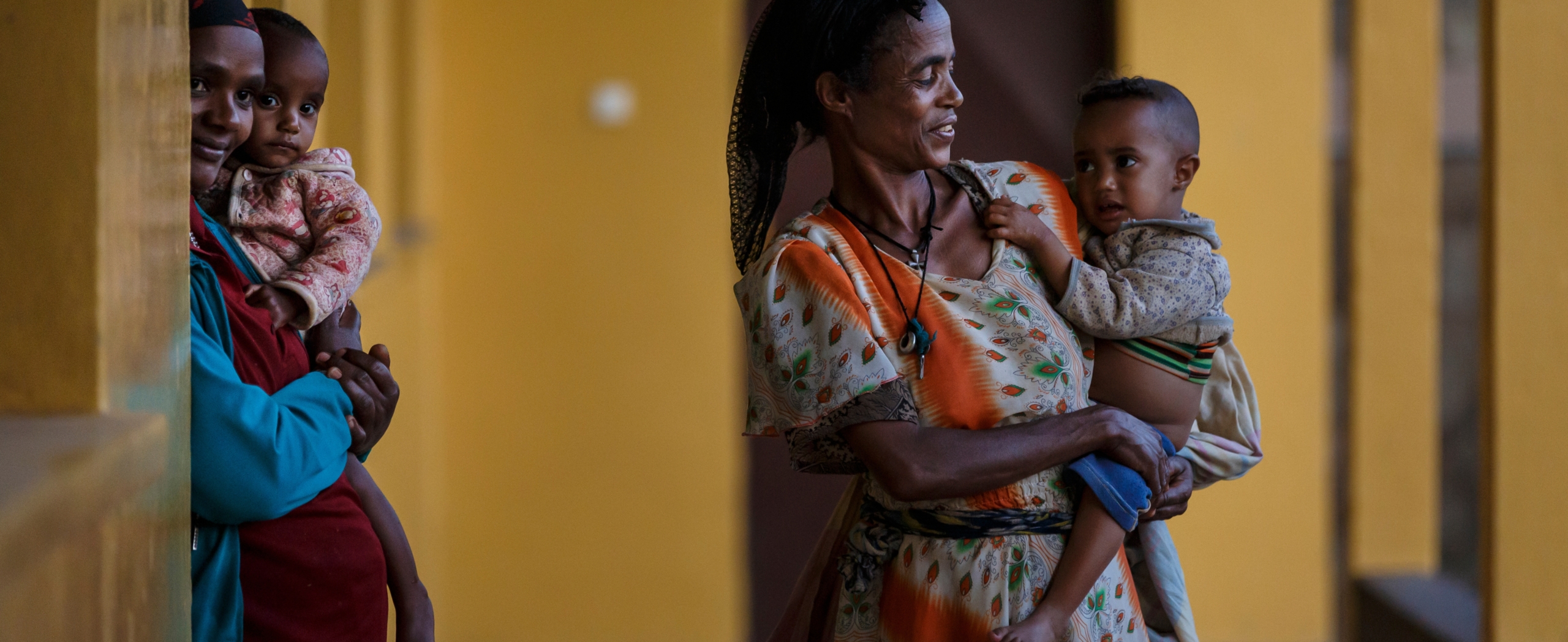 Zwei Frauen mit Kindern auf dem Arm stehen auf einem Gang.