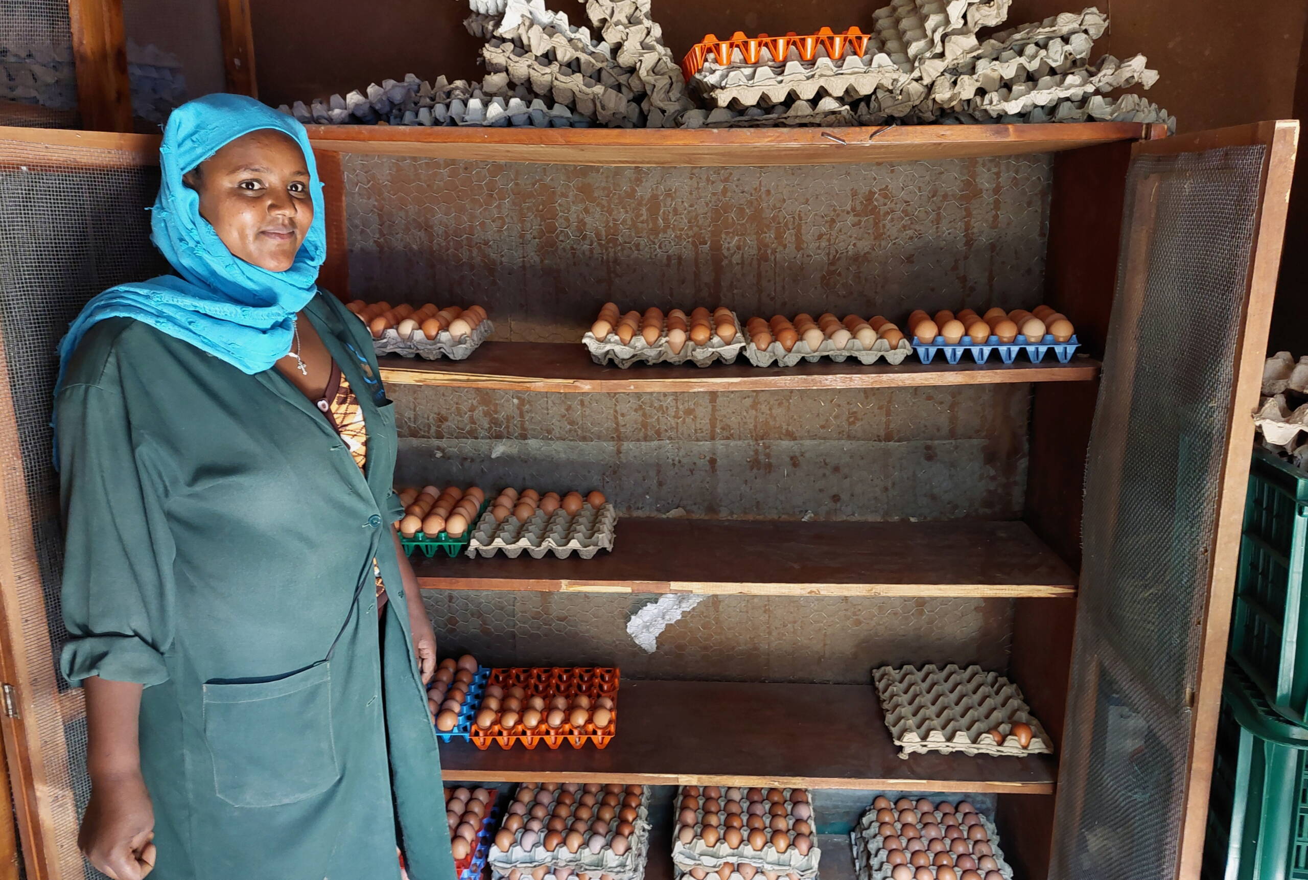 Eine Frau steht stolz vor einem Gestell mit Hühnereier.