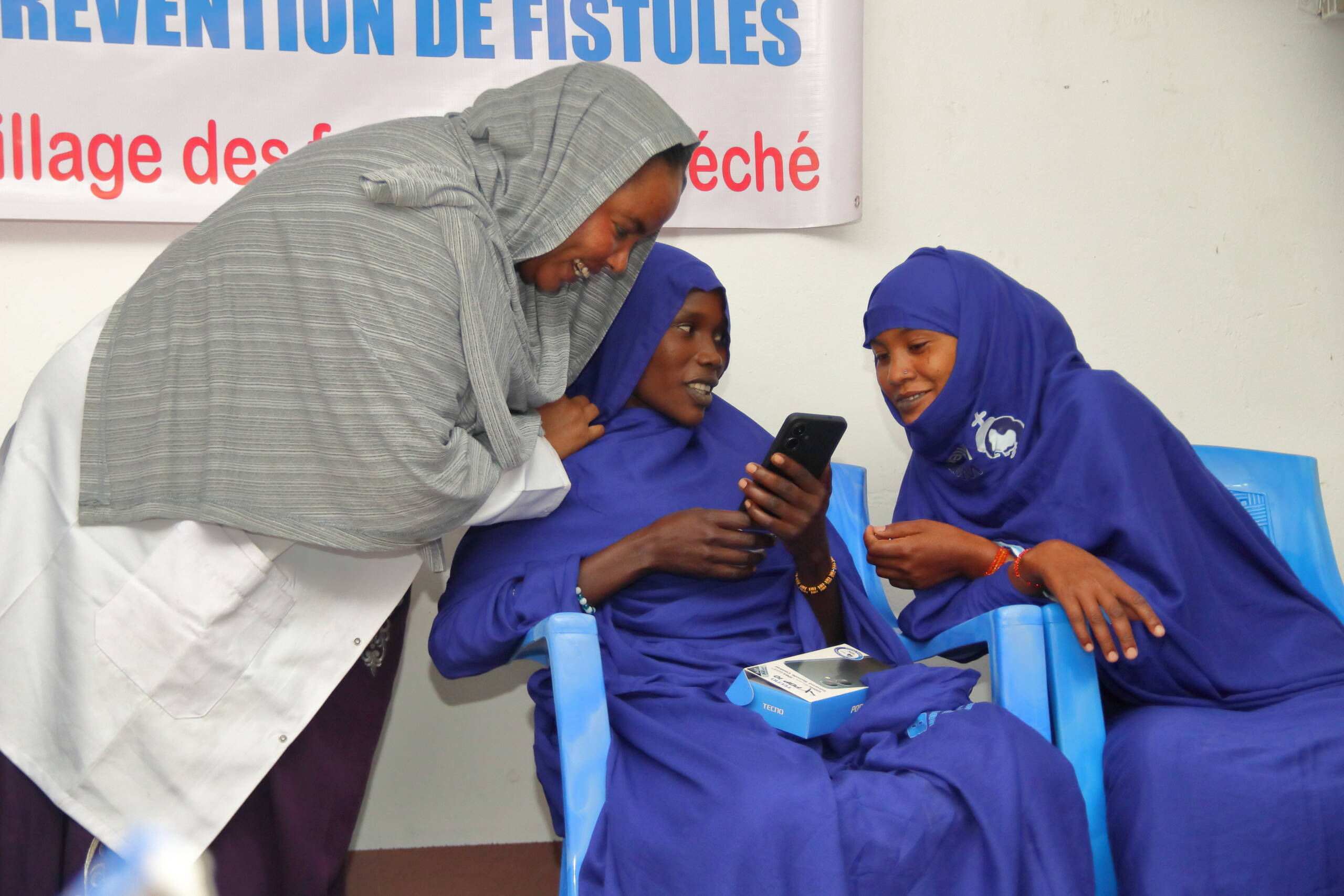 Drei Frauen beugen sich über ein Handy. Eine ist eine medizinische Fachperson