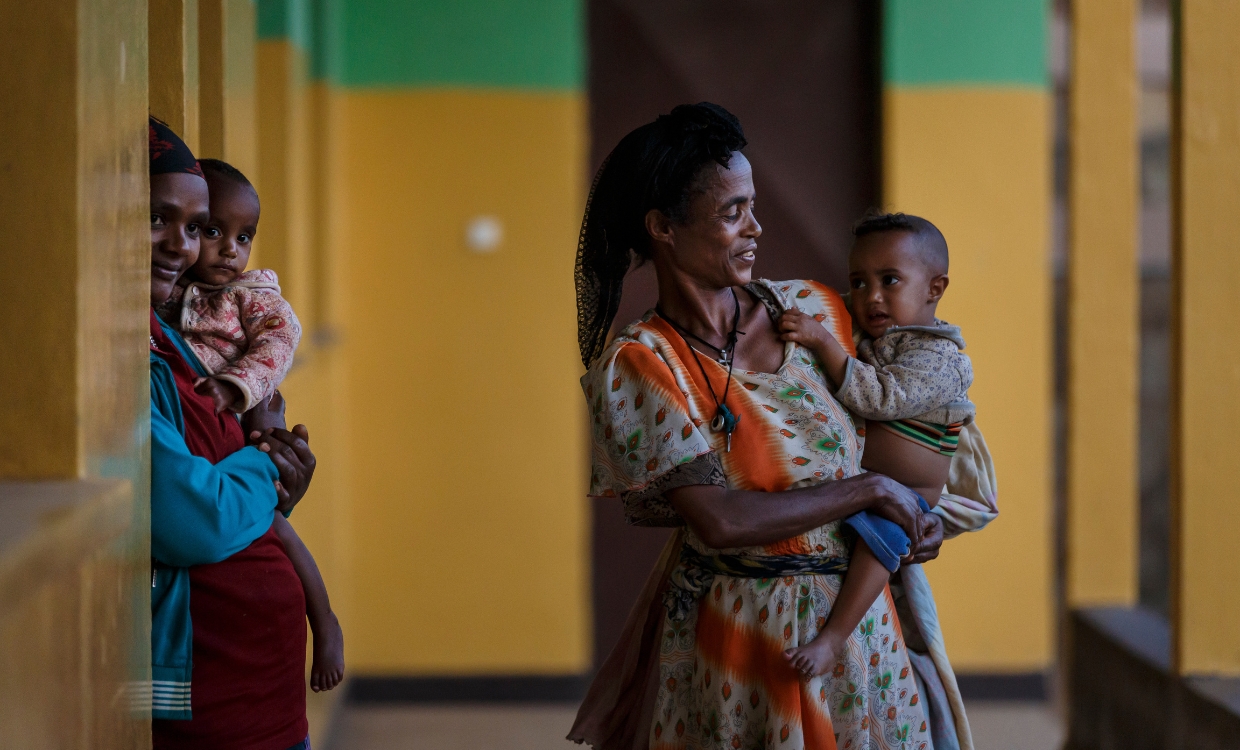 Frauen stehen auf einem Gang und tragen ihre Kinder auf den Armen.