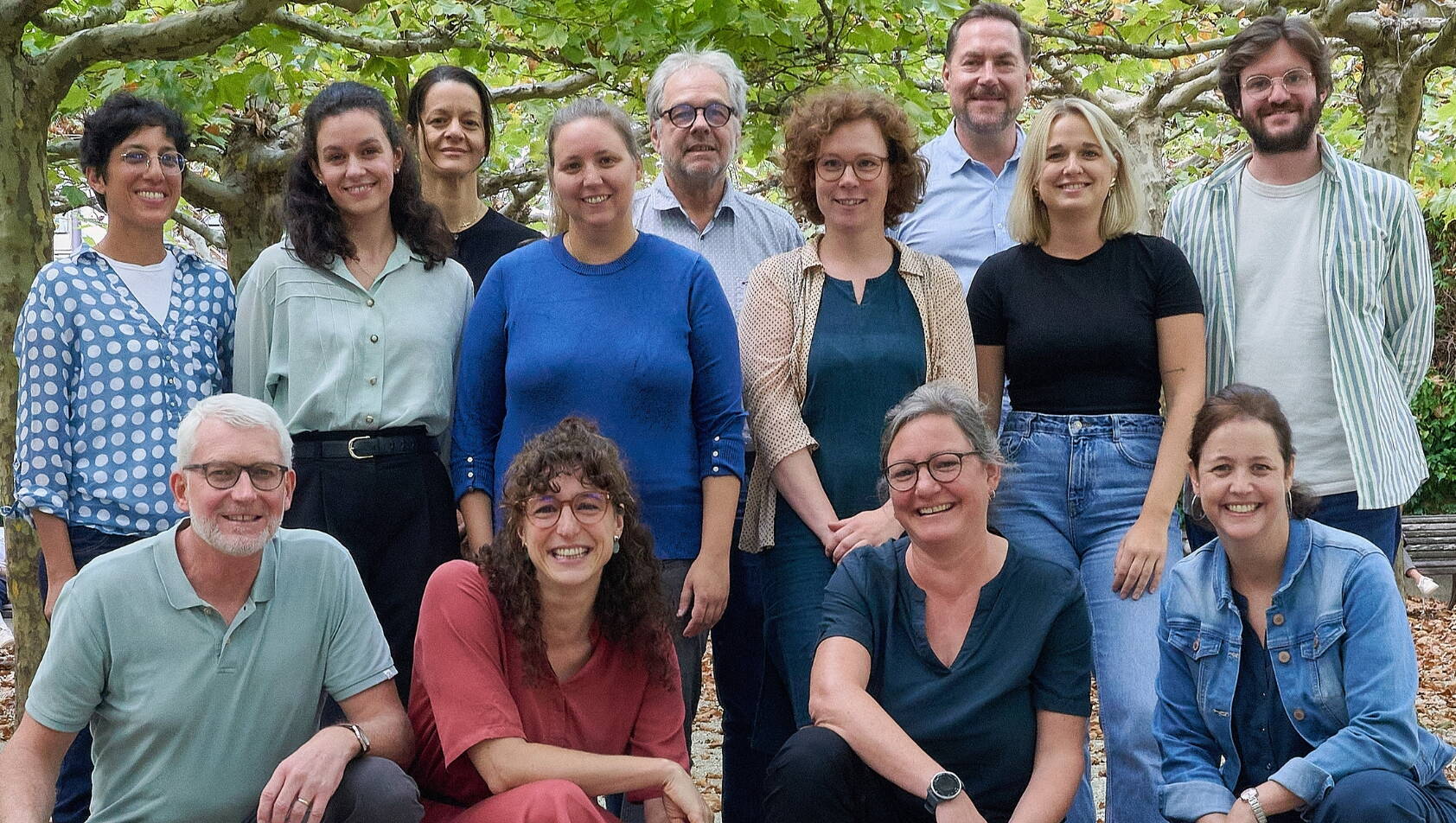 Team und Vorstand Menschen stehen unter Platanen und lachen.