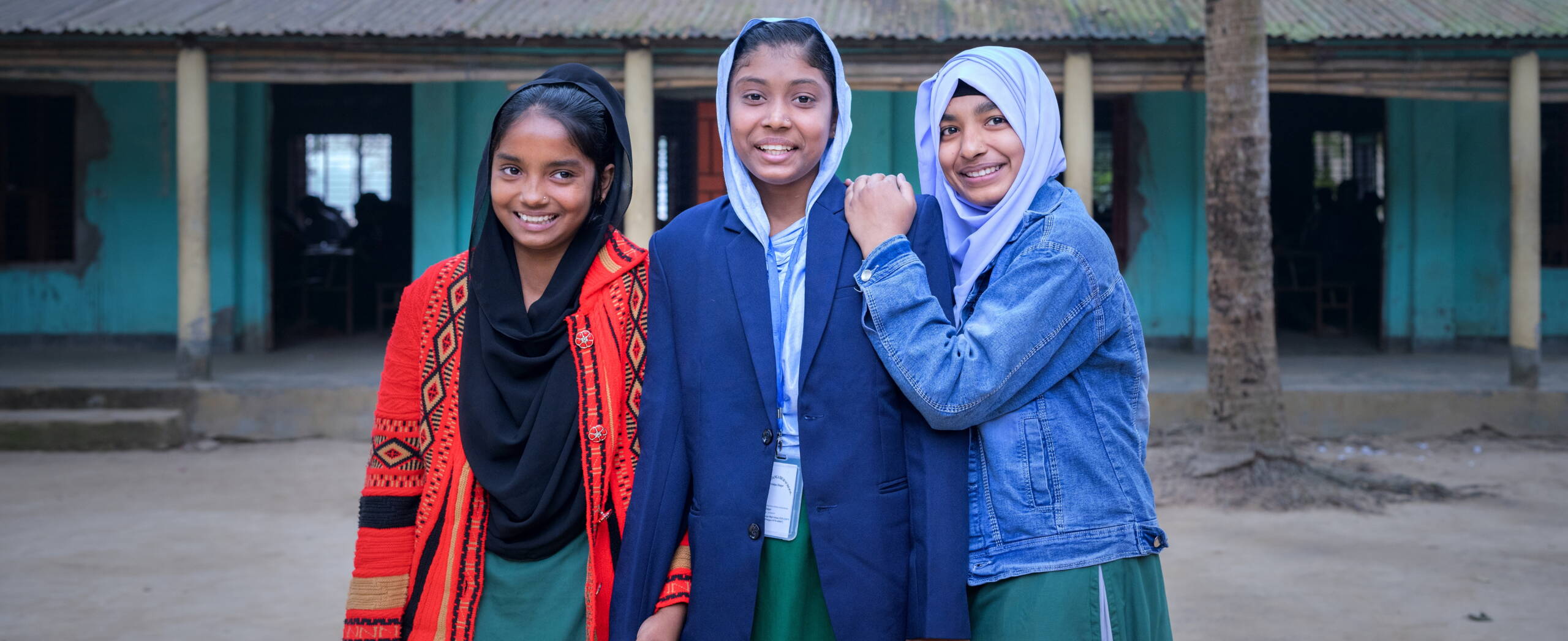 Drei Mädchen lehnen aneinander und schauen in die Kamera.