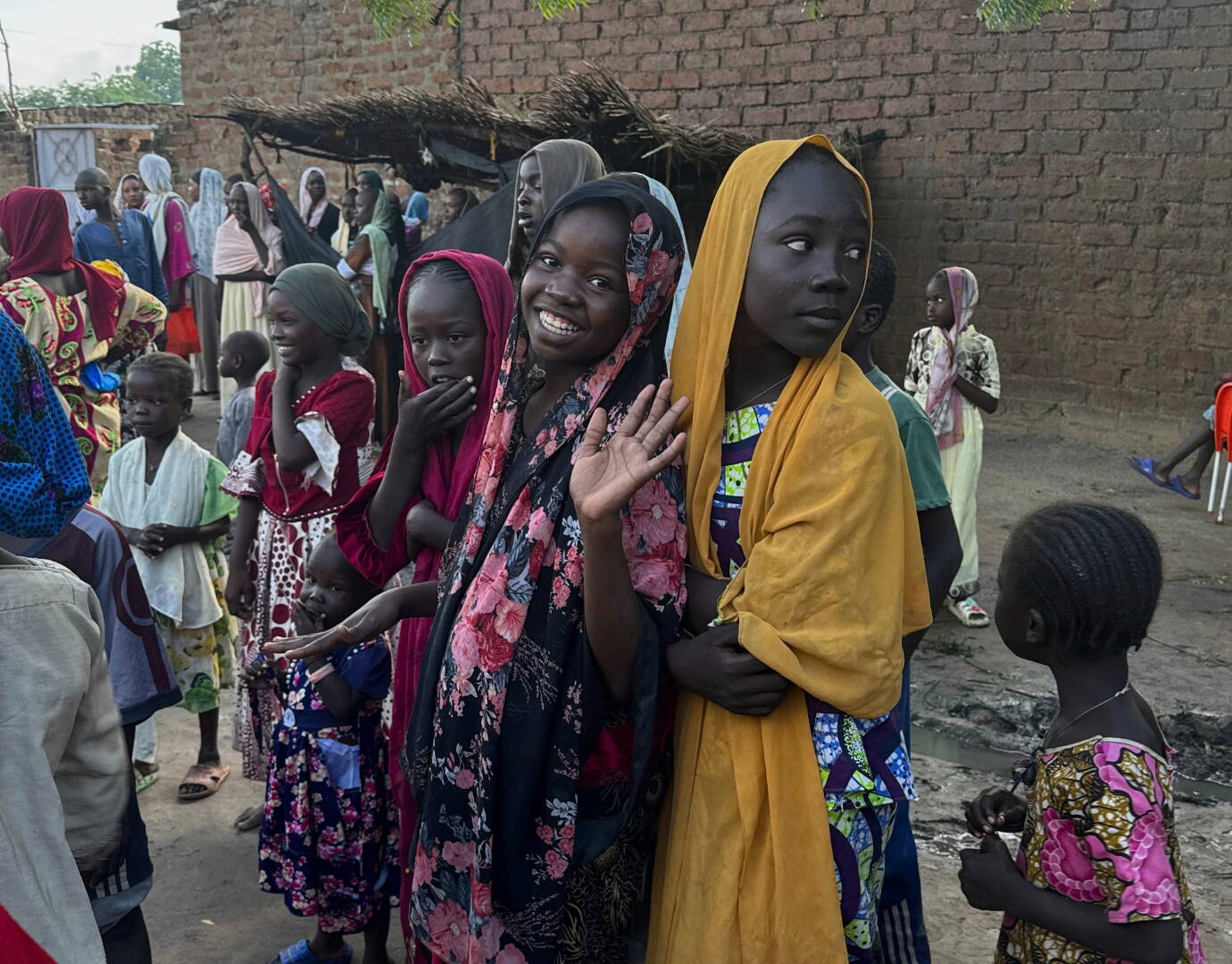 Jetzt spenden! Mädchen stehen in einer Reihe. Eines schaut in die Kamera und winkt.
