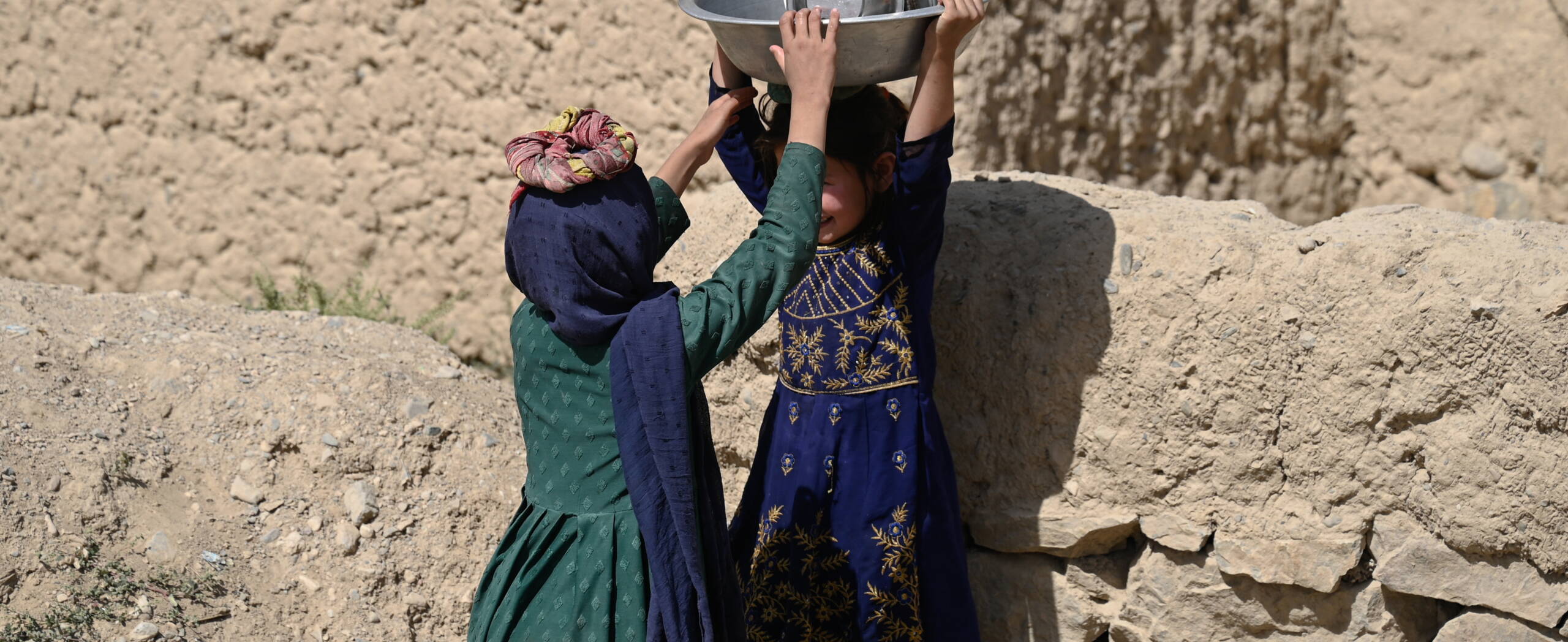 Mädchen Afghanistan Zwei Mädchen aus Afghanistan stehen sich gegenüber, eines trägt einen Kessel auf dem Kopf, das andere hält ihn.
