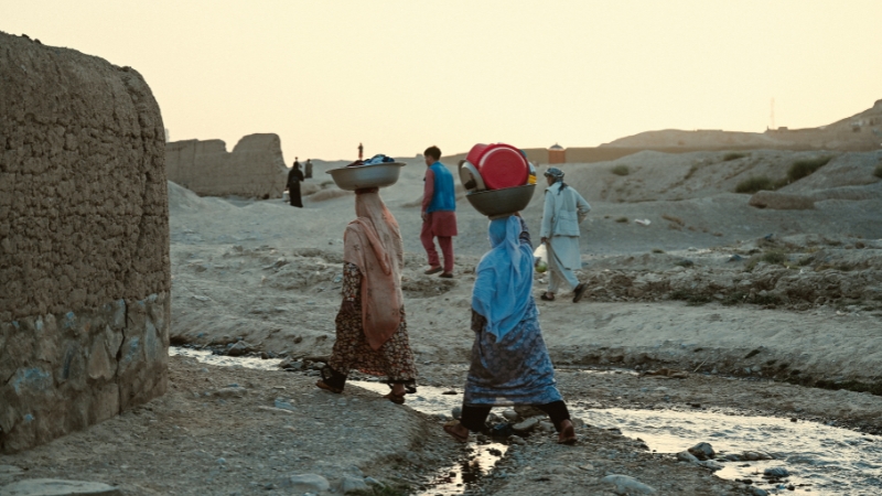 Mehrere afghanische Frauen tragen Gefässe auf dem Kopf.