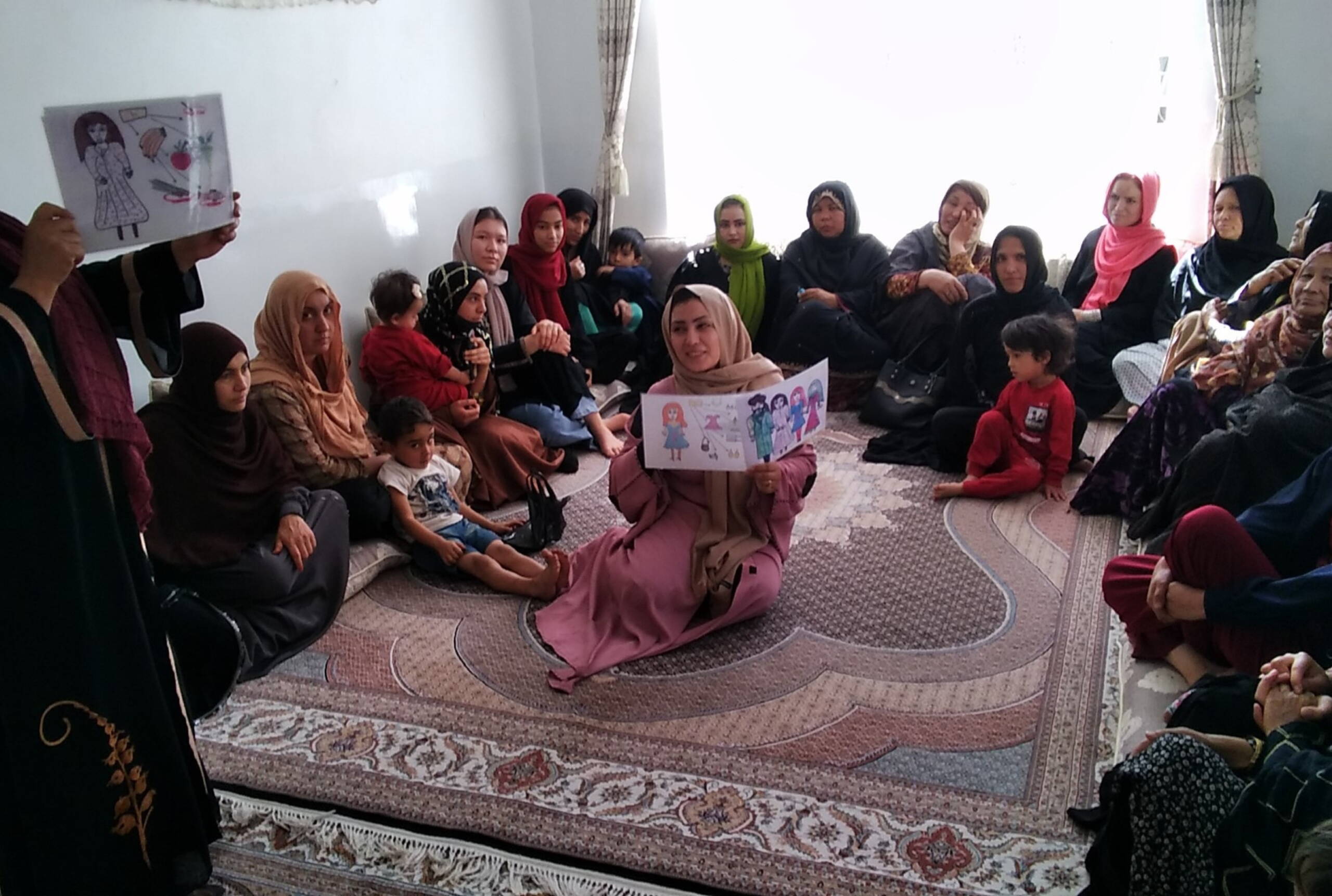 Frauen sitzen im Kreis, eine Frau sitzt in der Mitte und hält eine Zeichnung mit Kindern hoch.
