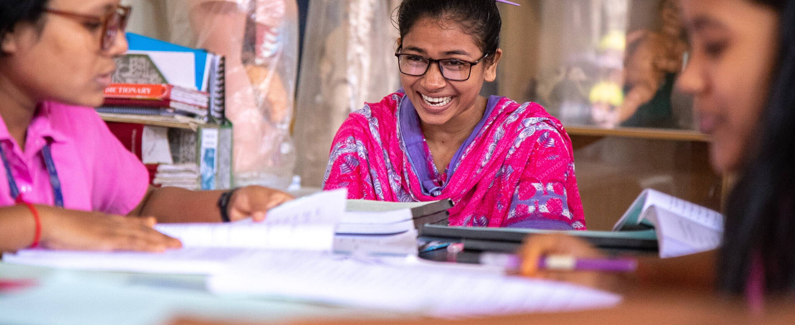 Frauen sitzen hinter Schreibblöcken an Tisch und lachen.