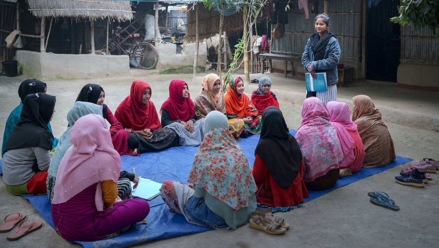 Mädchen sitzen auf dem Boden im Kreis, eine Frau steht vor ihnen.