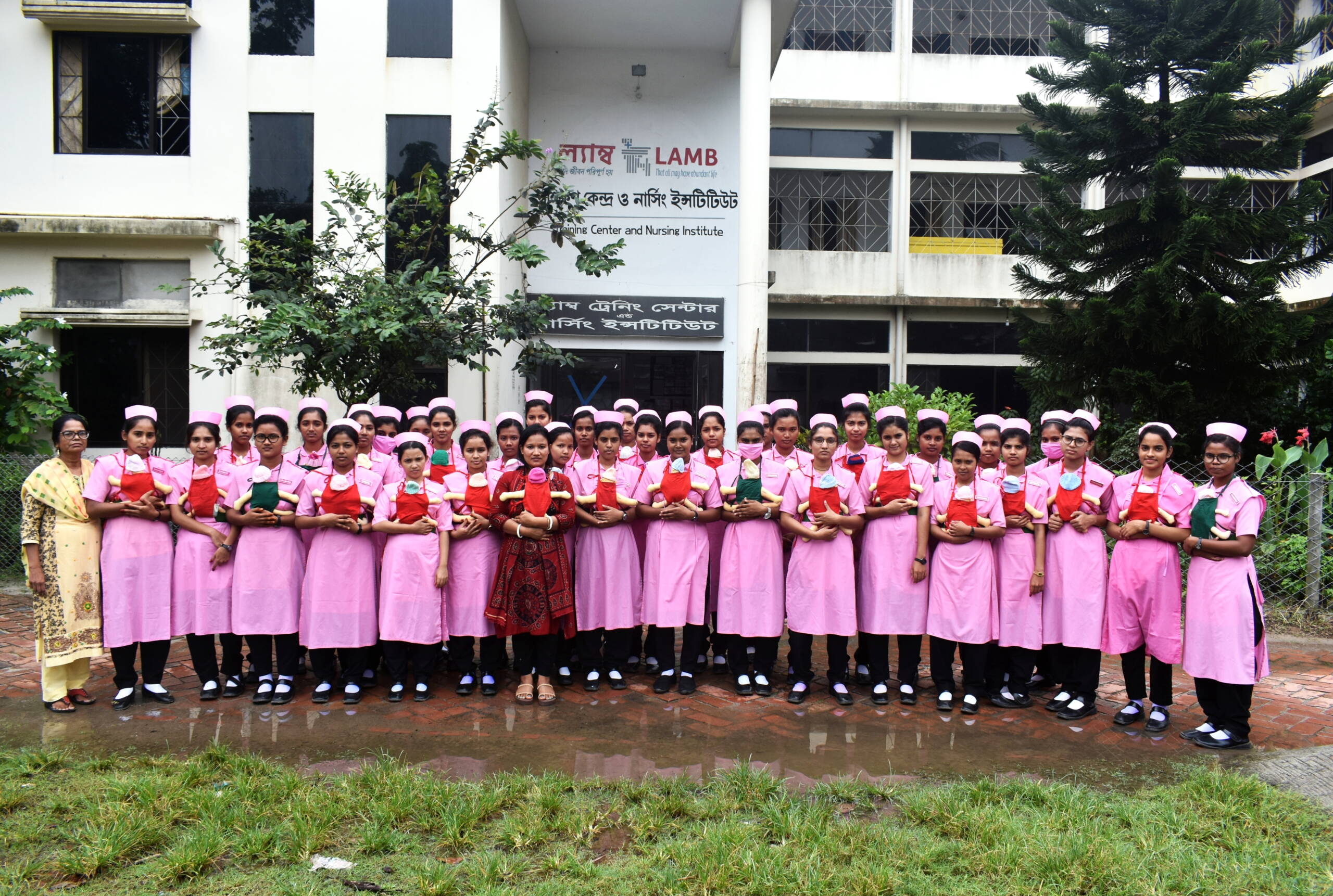 Eine Gruppe junger Frauen in rosaroter Kleidung steht beieinander, auf den Bäuchen haben sie Stoffpuppen umgebunden.