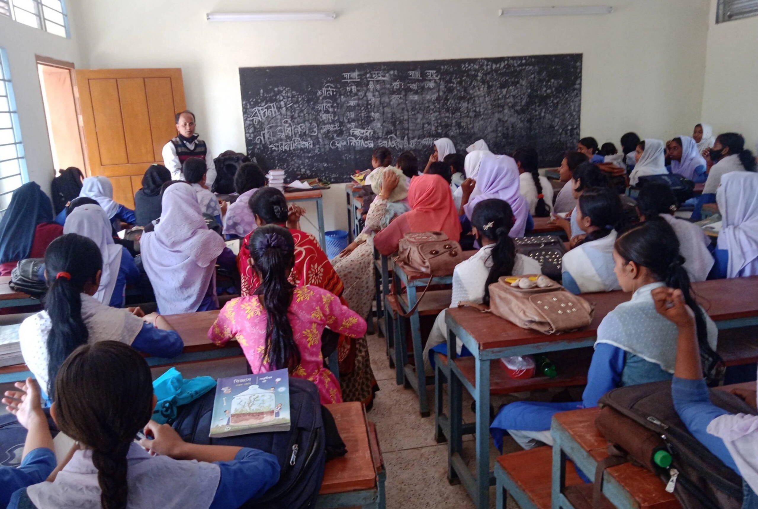 Ein Lehrer steht vor einer Klasse mit Mädchen und erklärt etwas.