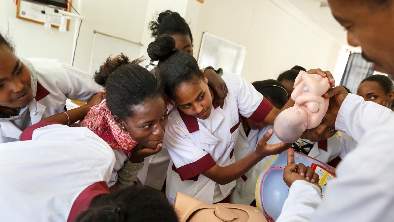 Hebammenstudentinnen beugen sich zu einer Baby-Puppe.