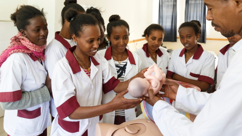Hebammenausbildung Mehrere junge Frauen stehen um eine Ausbildungspuppe.