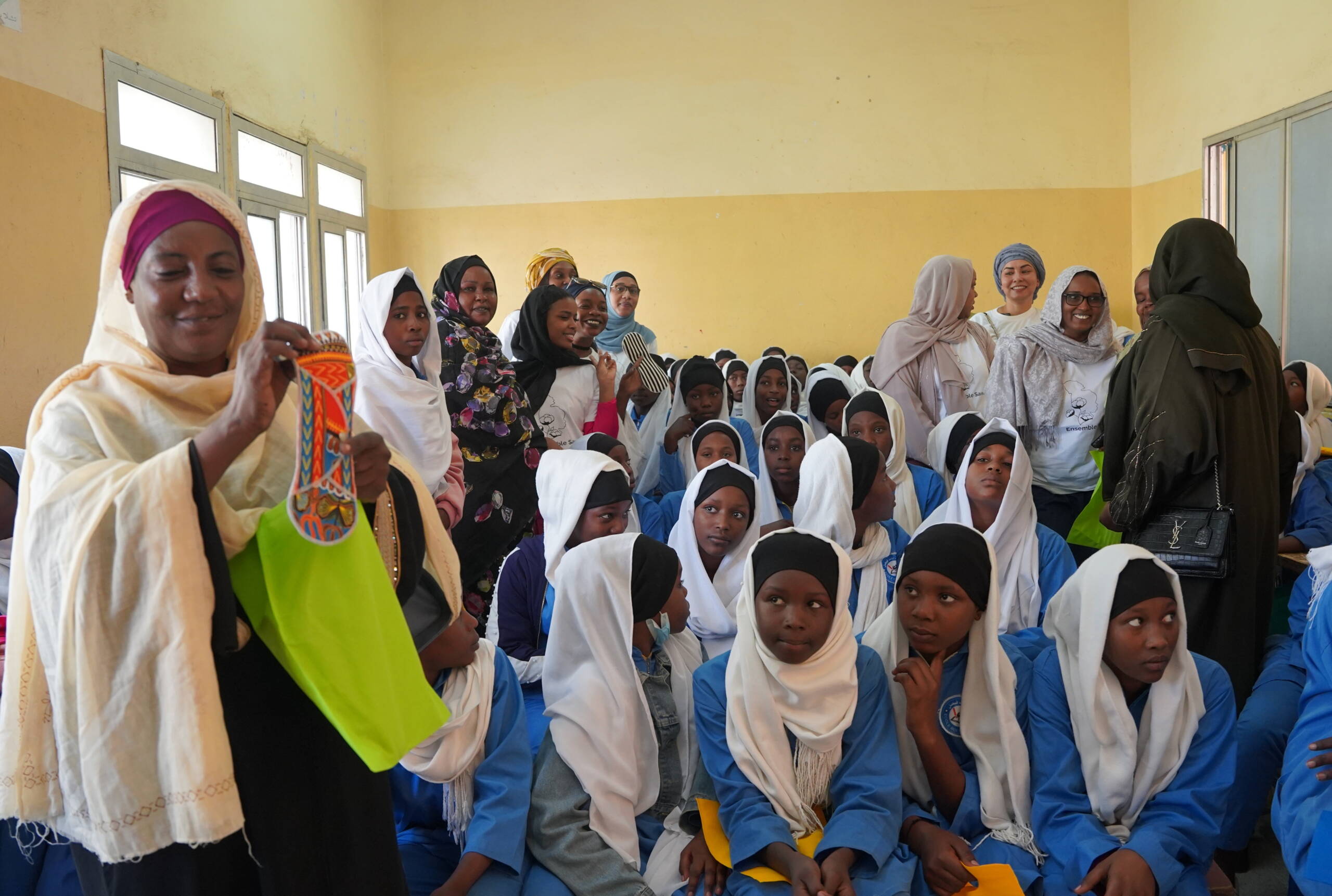 Sensibilisierung Eine Frau hält eine wiederverwendbare Stoffbinde vor einer Klasse in die Luft.