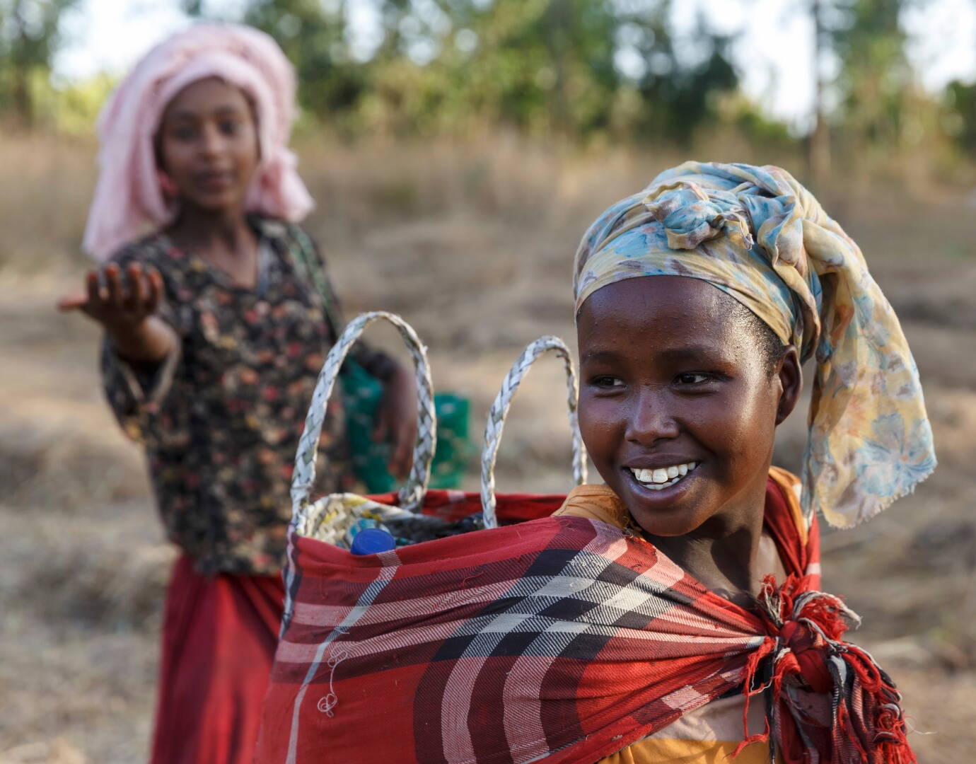 Jetzt spenden! Lachende Frau aus Äthiopien trägt etwas auf dem Rücken.