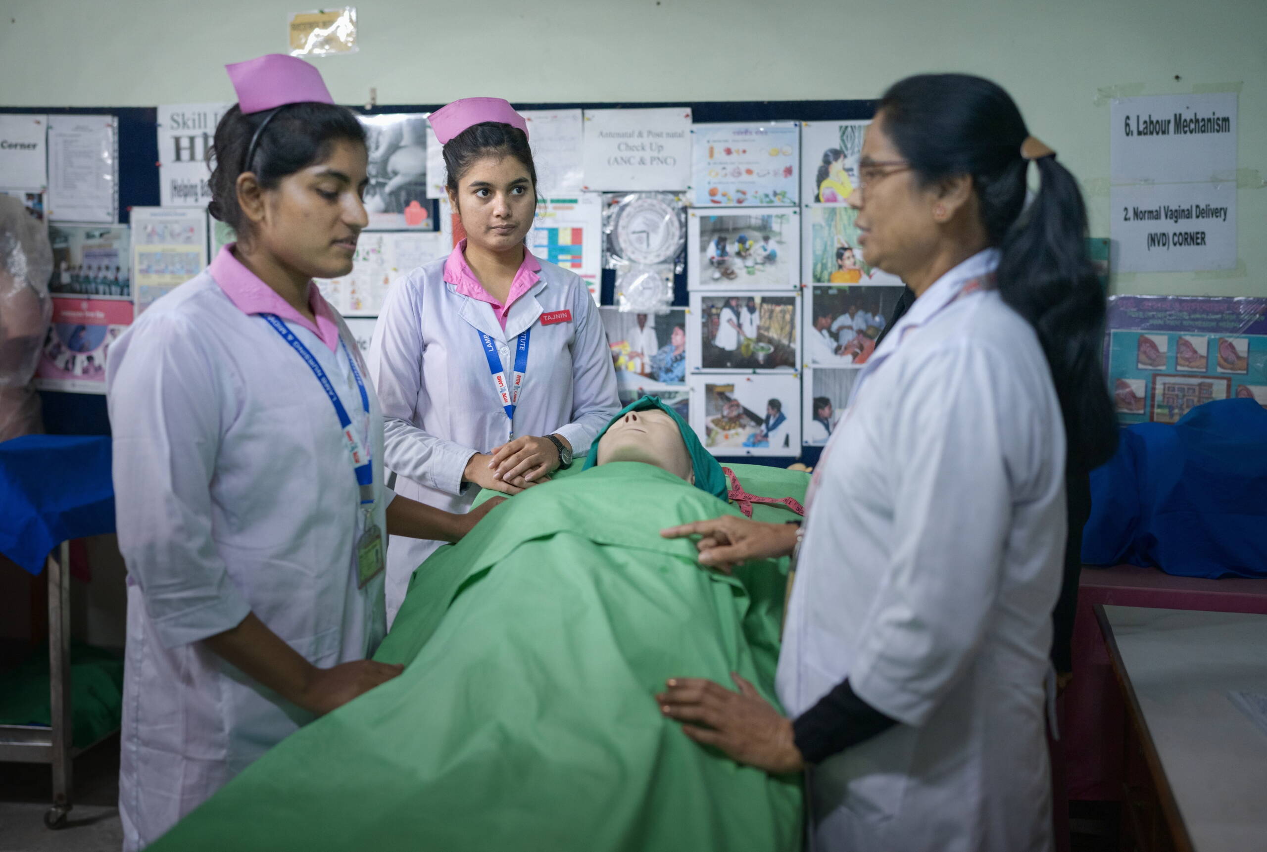 Eine Fachfrau redet mit zwei Studentinnen, während sie sich über eine Puppe beugen.