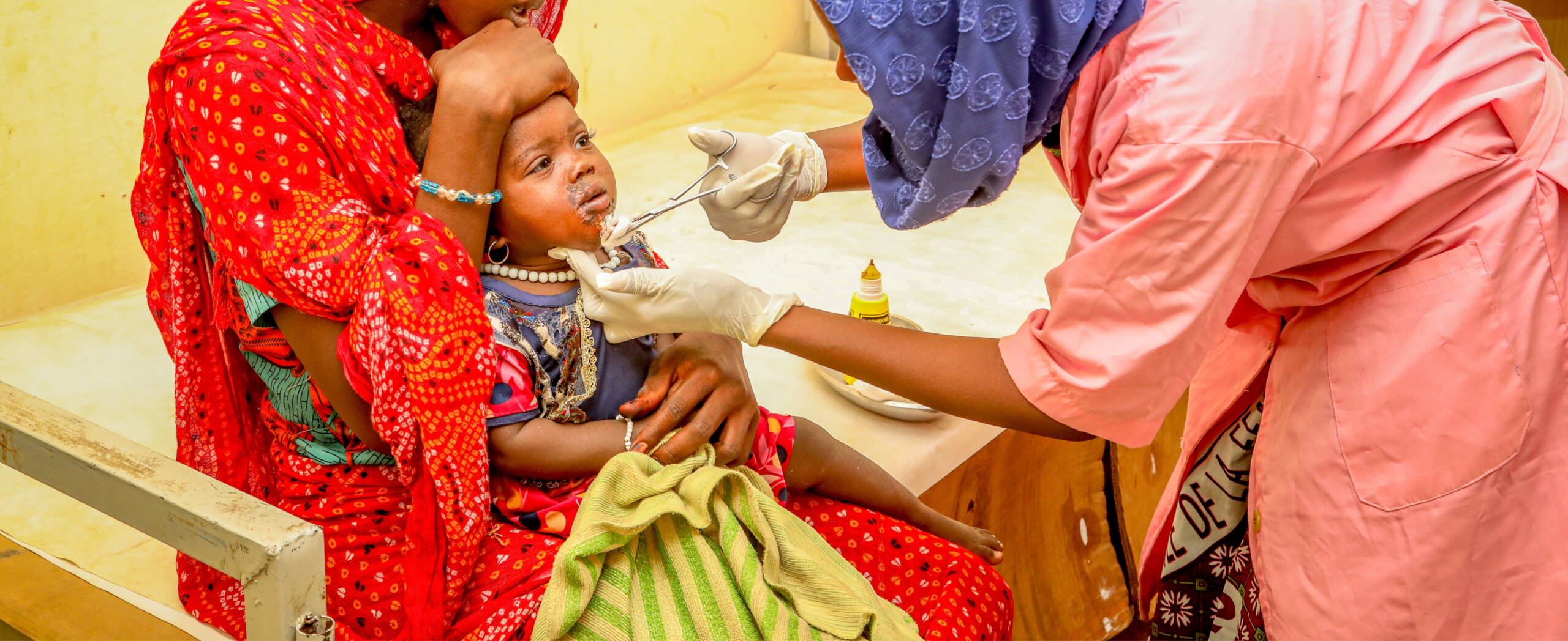 Eine Hebamme tupft mit Watte auf eine Wunde im Gesicht eines kleinen Mädchens.