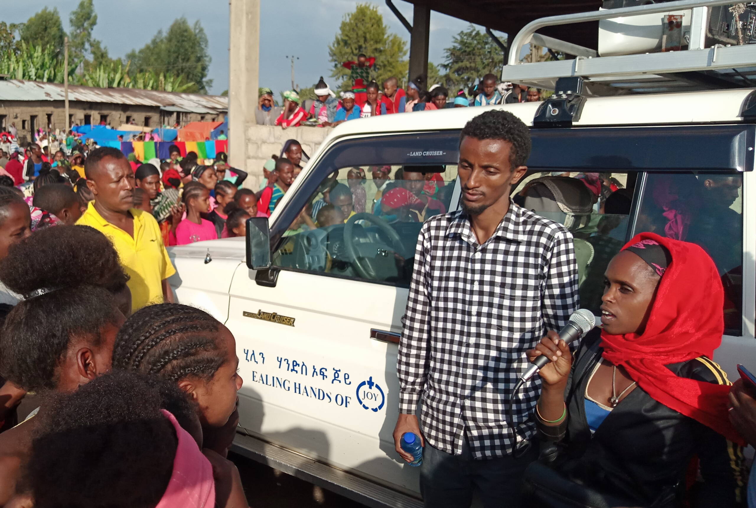 Eine Frau steht vor einem Auto auf dem Markt und spricht in ein Mikrofon.