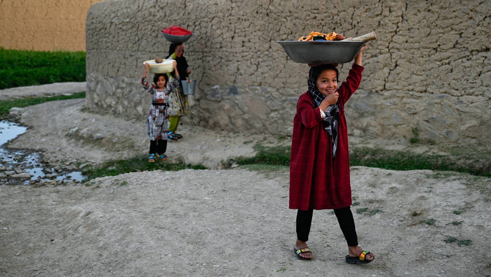 Mädchen Afghanistan Mädchen laufen einer Mauer entlang und tragen Schüsseln auf dem Kopf.