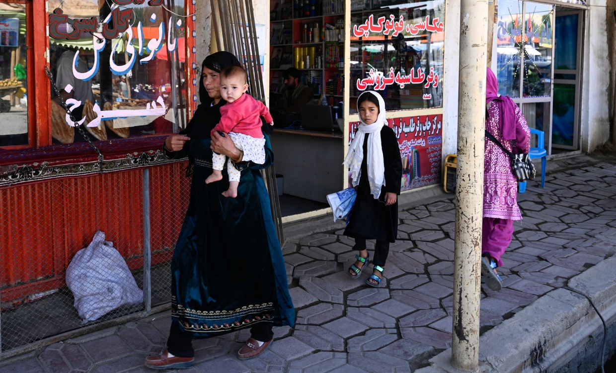 Eine Frau mit Kind auf dem Arm läuft eine Einkaufspassage entlang.