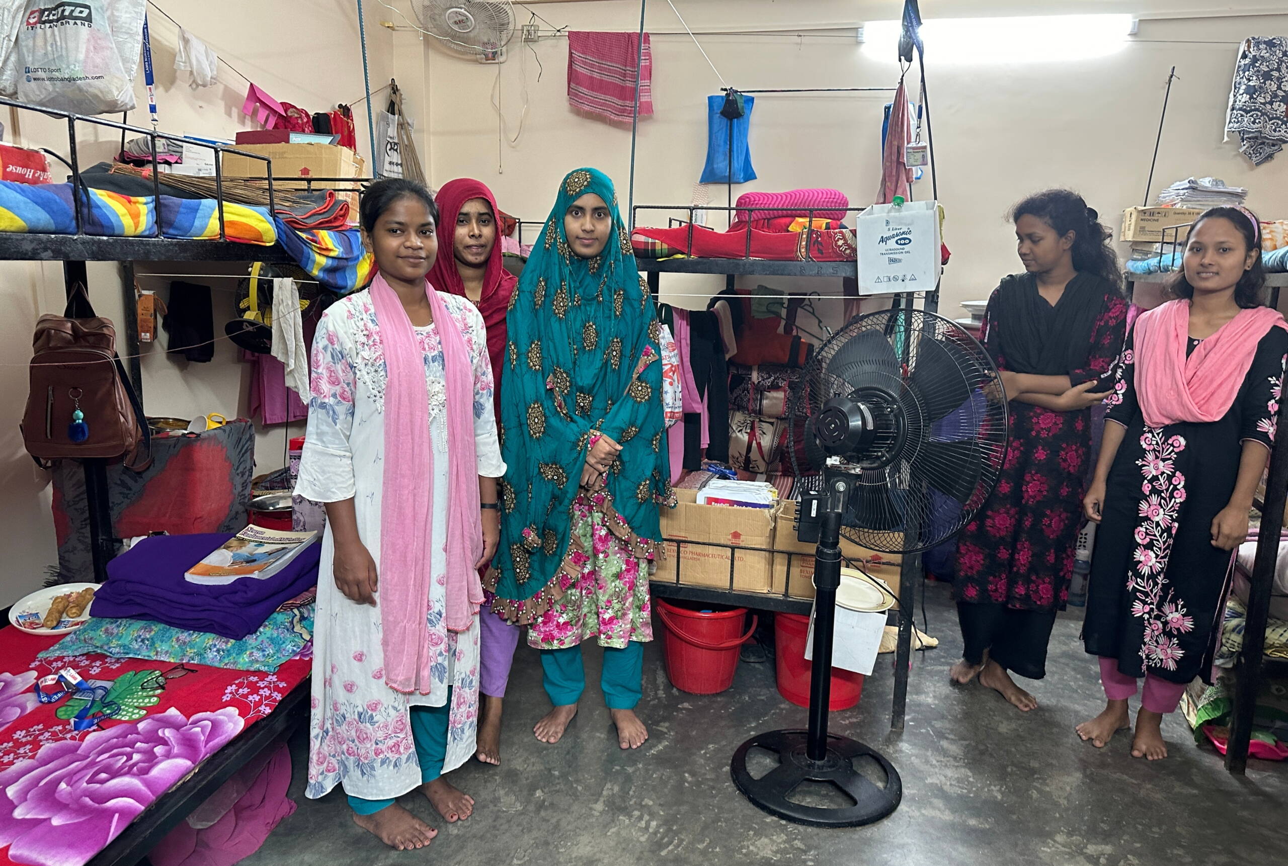 Frauen stehen in einem Schlafsaal vor Stockbetten.
