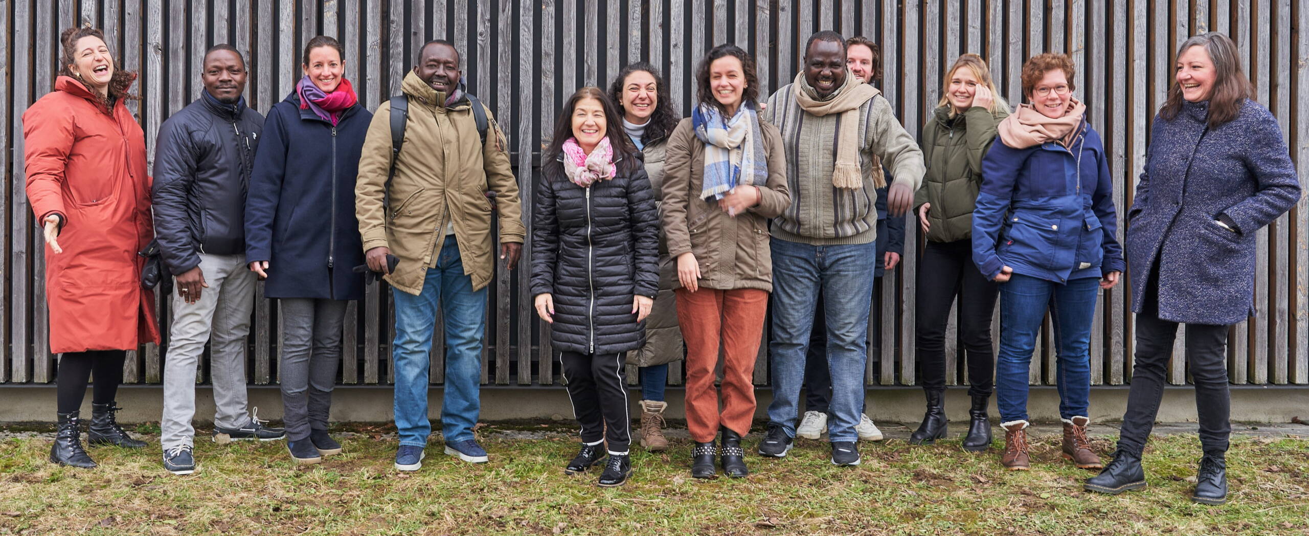 Menschen stehen vor einer Wand und lachen in die Kamera.