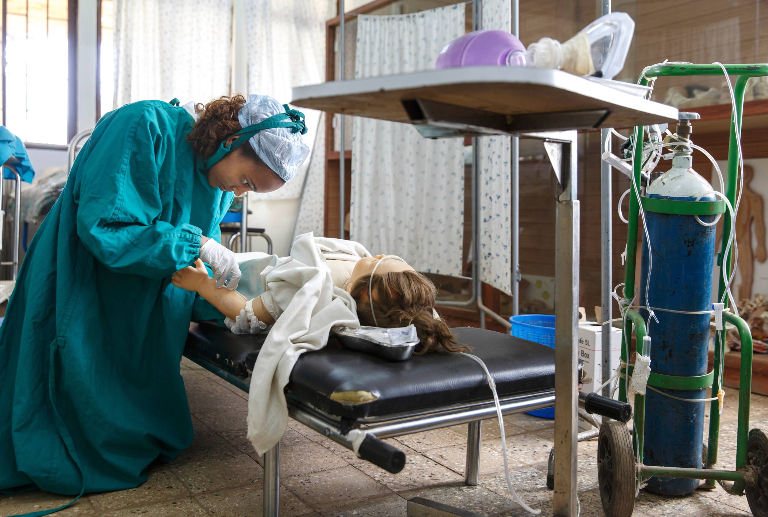 Eine Studentin kniet neben einer Tragbahre und untersucht eine Plastikpuppe.