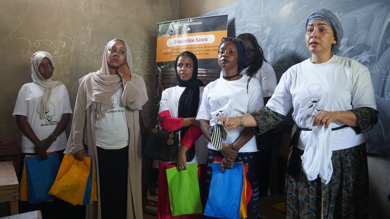 Ensemble Sawa Frauen stehen vor einer Klasse und sprechen zum Thema Menstruationshygiene.