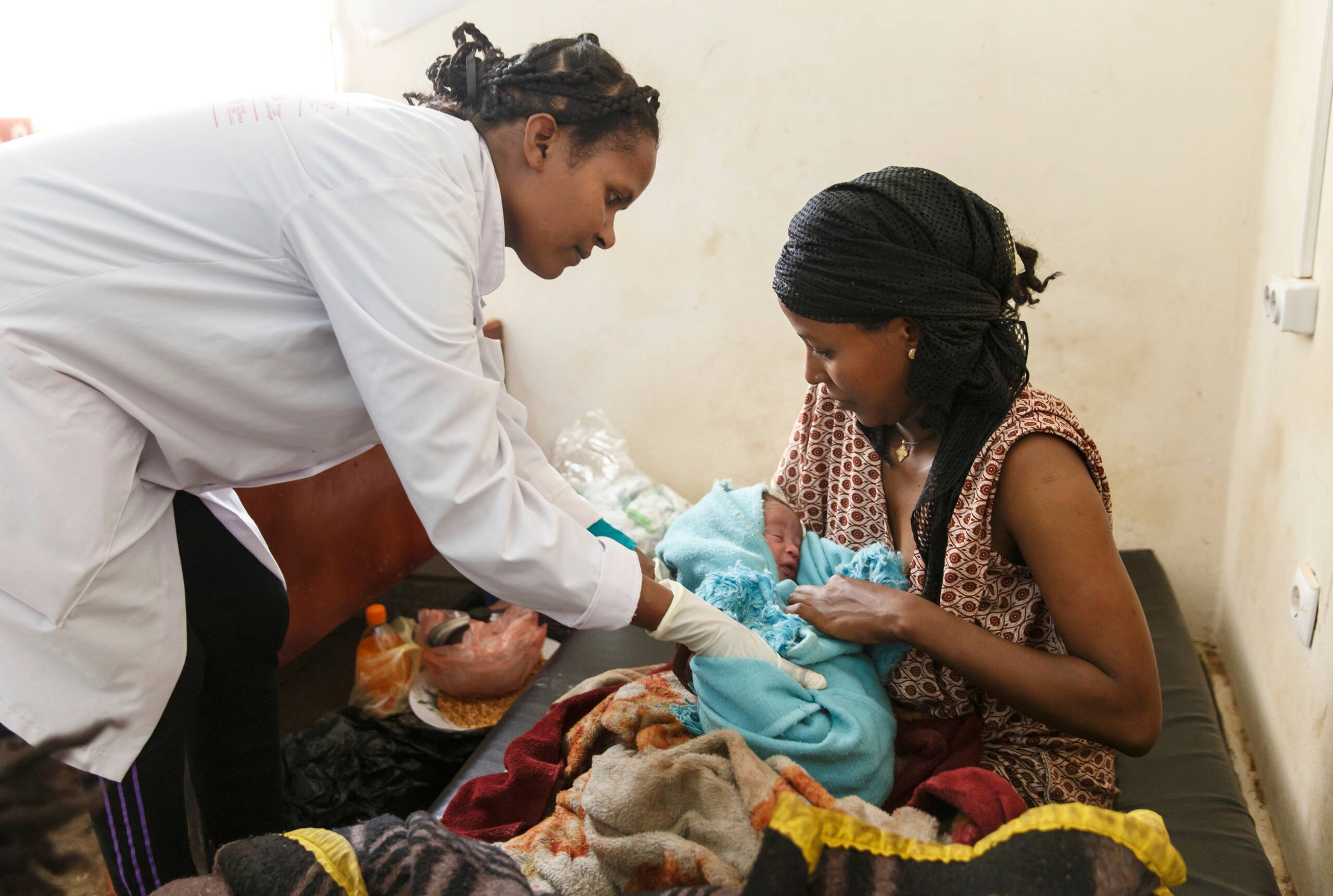 Eine Hebamme beugt sich über das Neugeborene, das in den Armen der Mutter liegt.