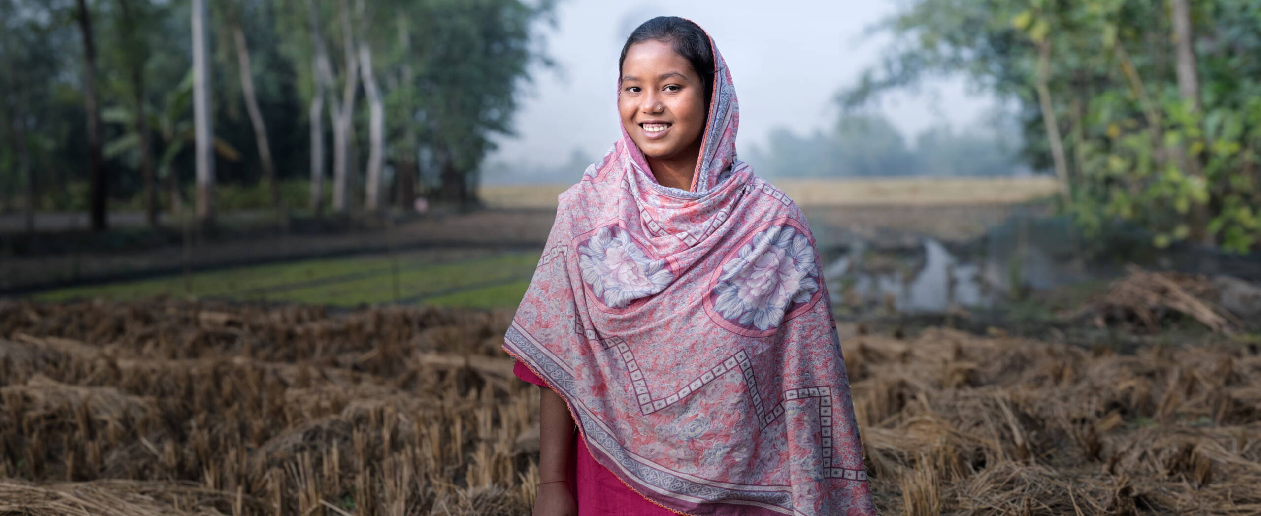 Ein Mädchen steht vor einem Kornfeld und lacht stolz in die Kamera.
