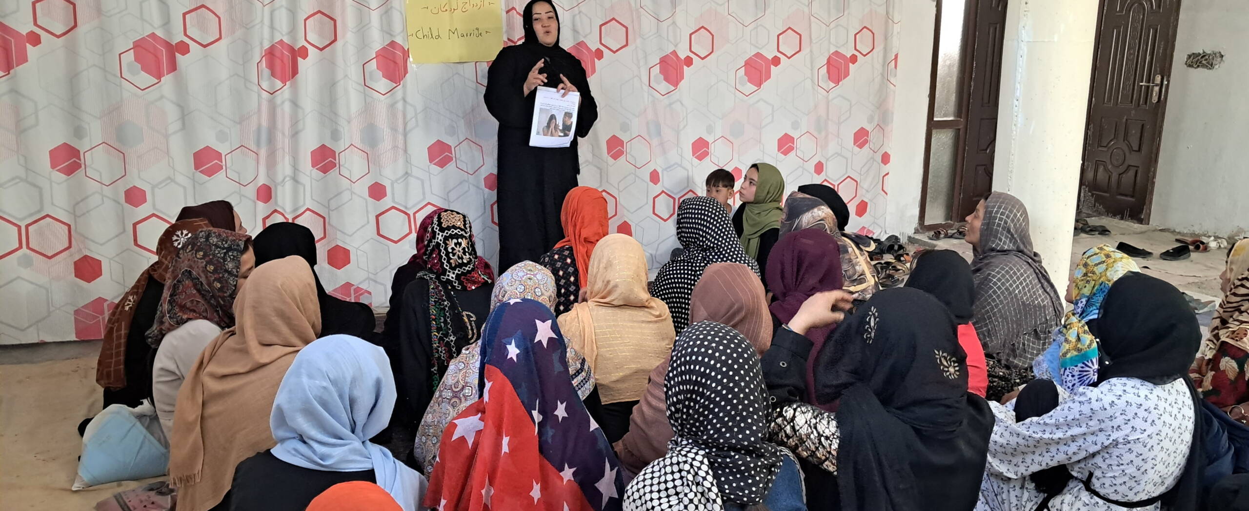 Eine Frau erklärt stehend etwas vor einer Gruppe sitzender Frauen.