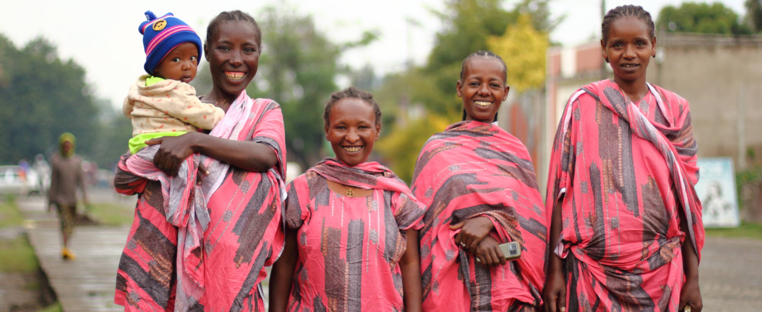 Vier Frauen stehen nebeneinander und lachen in die Kamera. Eine hat ein Kleinkind auf den Armen.