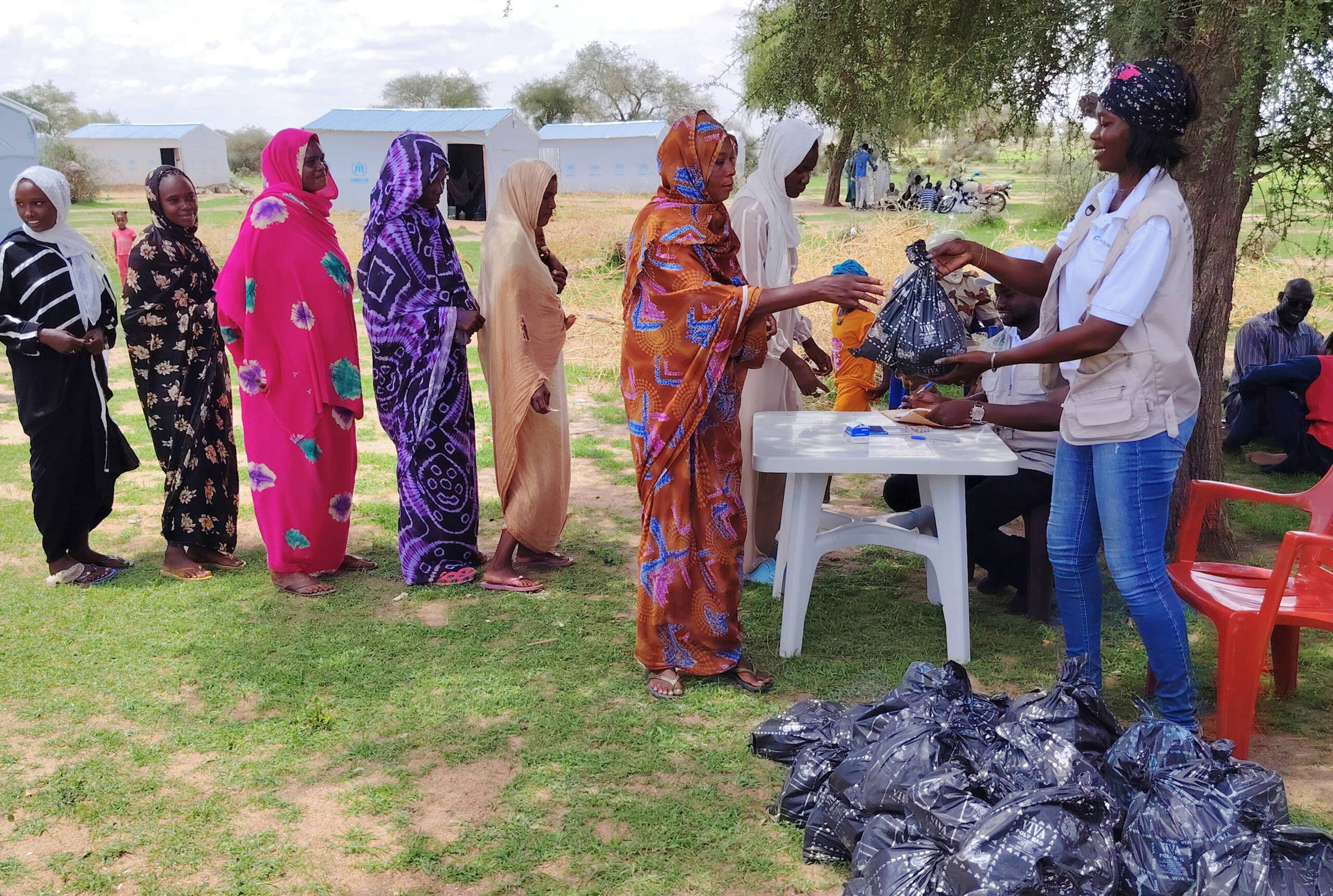 Frauen stehen Schlange; eine Frau hinter einem Tisch verteilt schwarze Plastiksäcke.