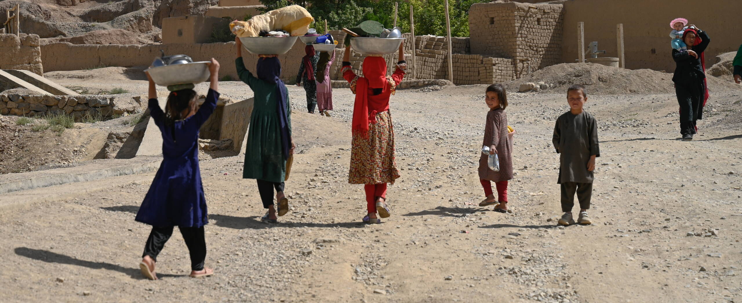 Mädchen laufen durch die Strasse und tragen grosse Metallgefässe auf dem Kopf.