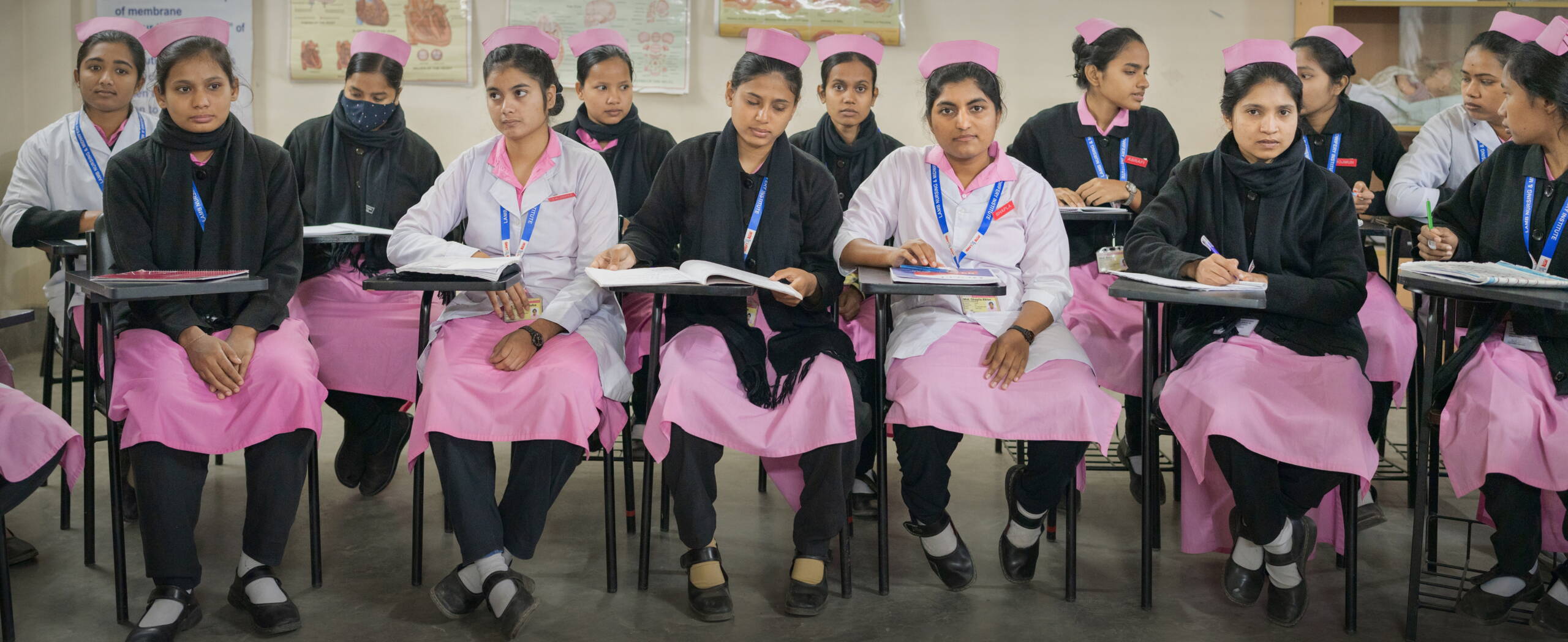 Junge Frauen sitzen auf Stühlen, vor sich kleine Pulte mit Lehrbüchern.