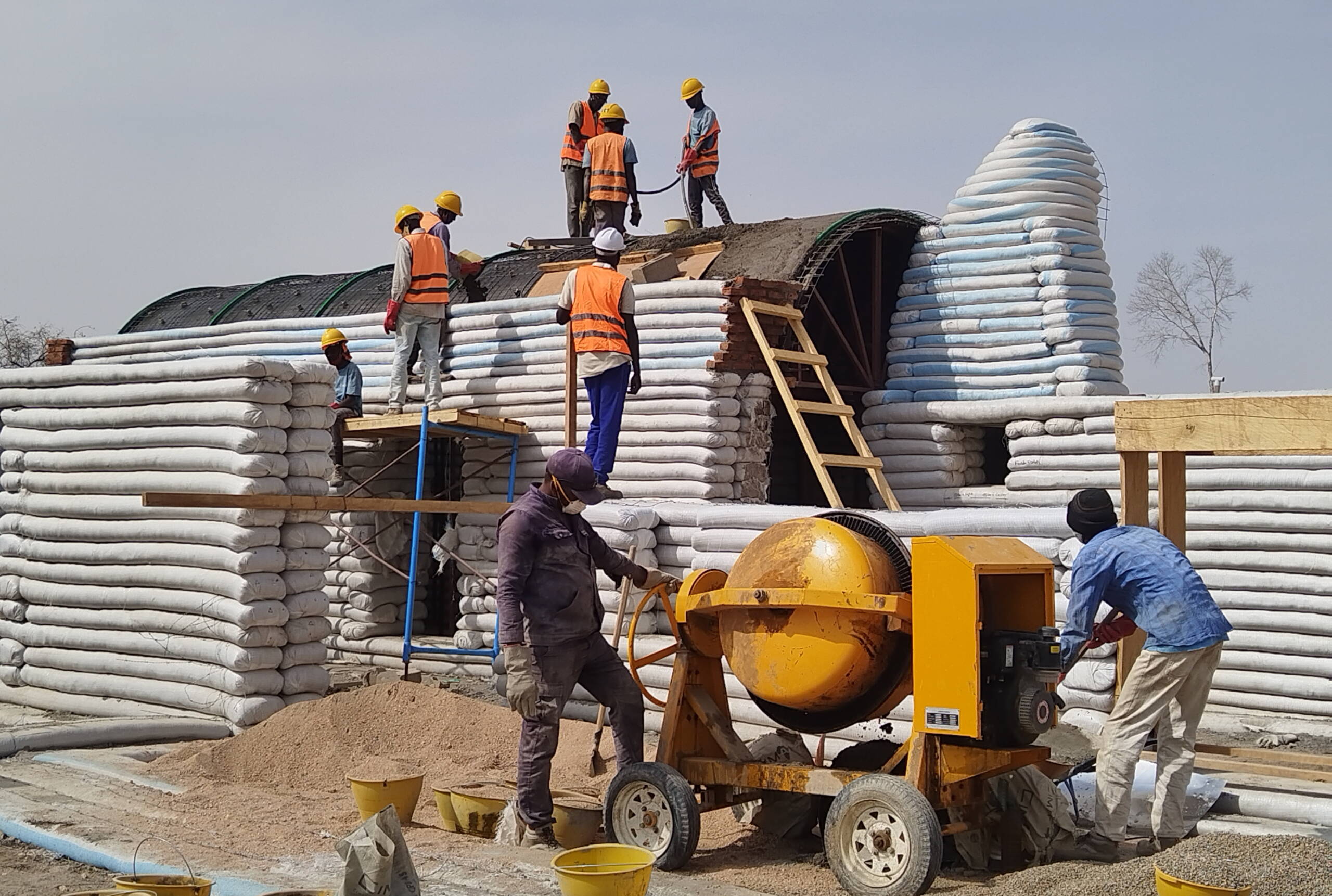 Bauarbeiter arbeiten an einem Gebäude, das aus geschichteten Sandsäcken besteht.