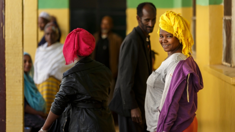 Eine Frau in einer Warteschlange dreht sich um und lacht in die Kamera.
