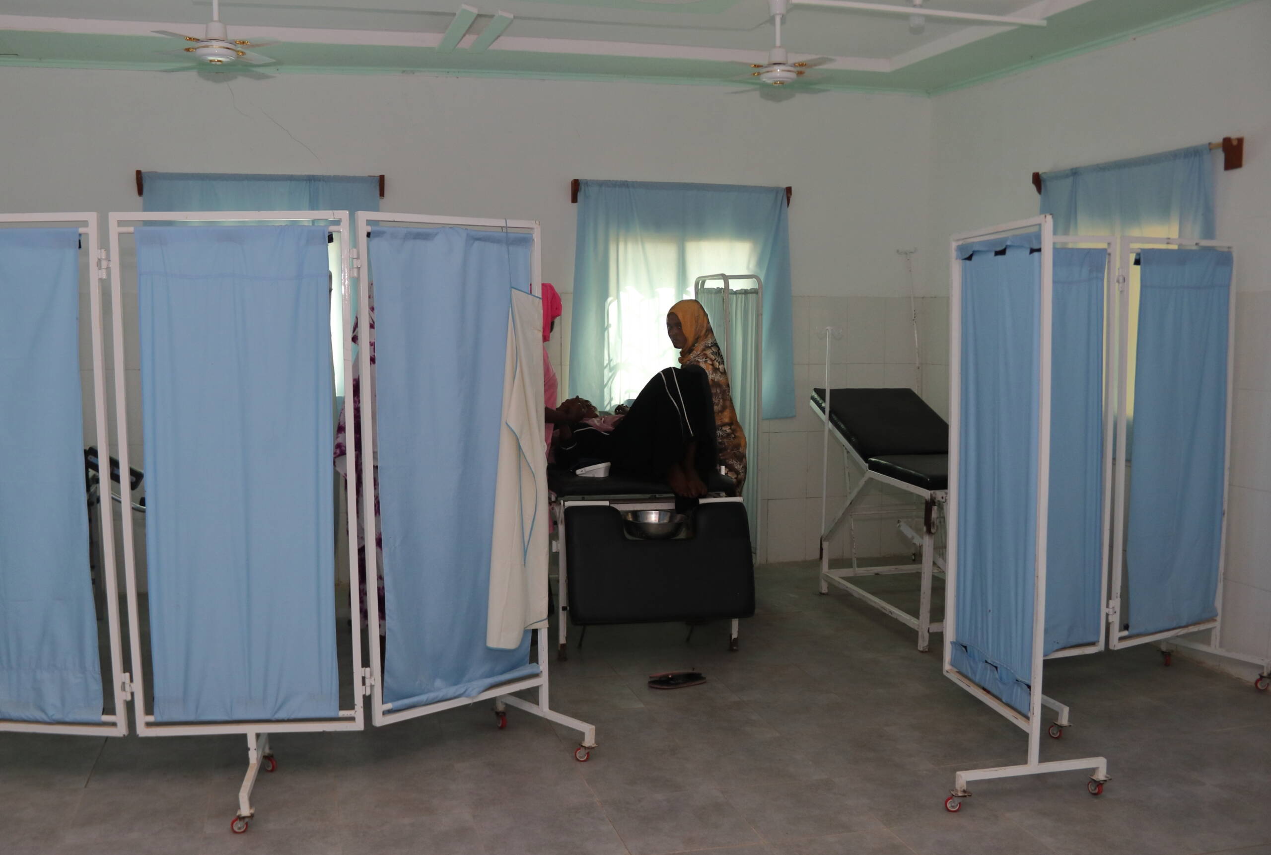 Raum mit Stellwänden, Liegen und gefliestem Boden.