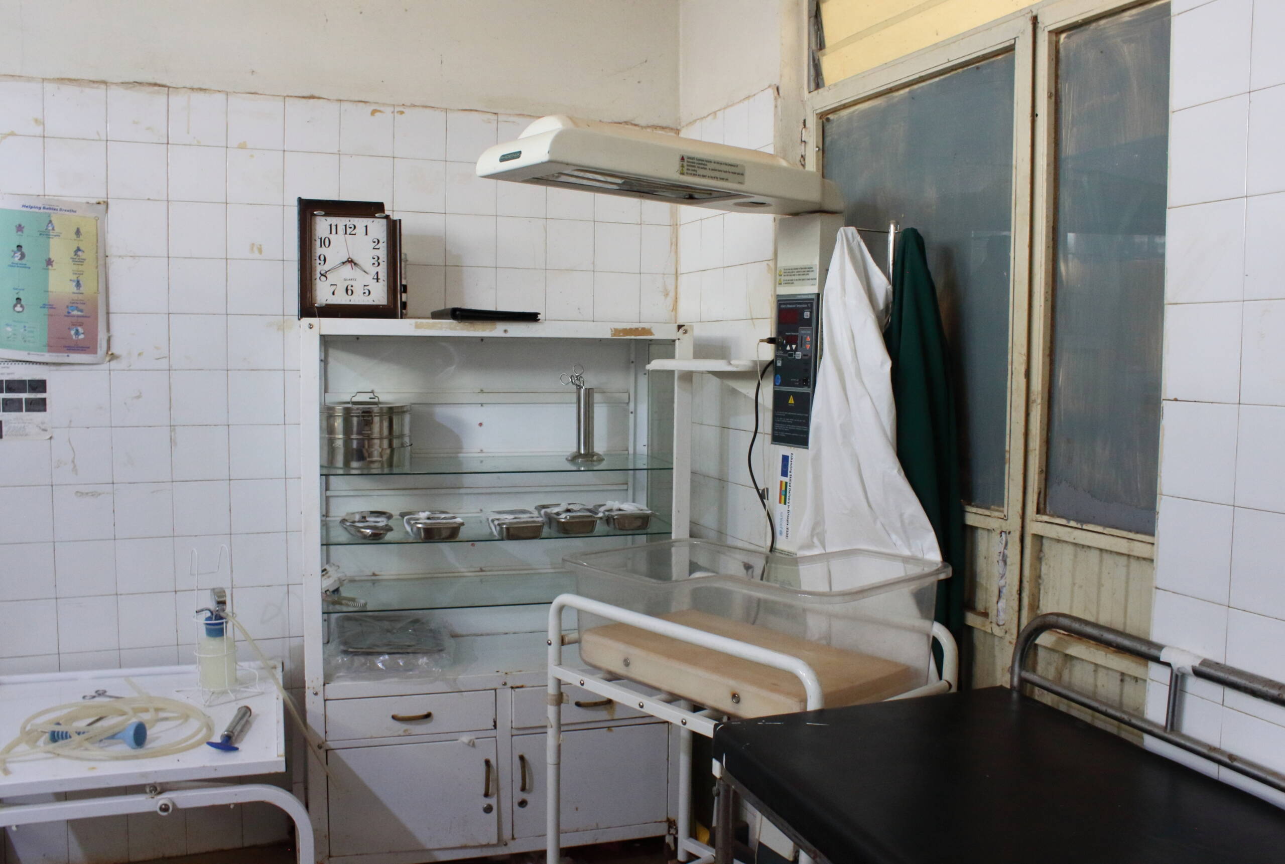 Zimmer mit gefliesten Wänden, einem Wärmebettchen und medizinischem Equipment. 